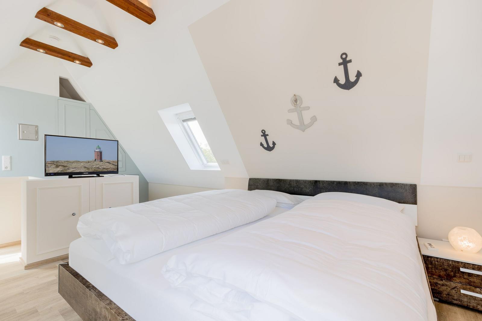 Schlafzimmer mit Dachbodenfenster, Bett und Fernseher.
