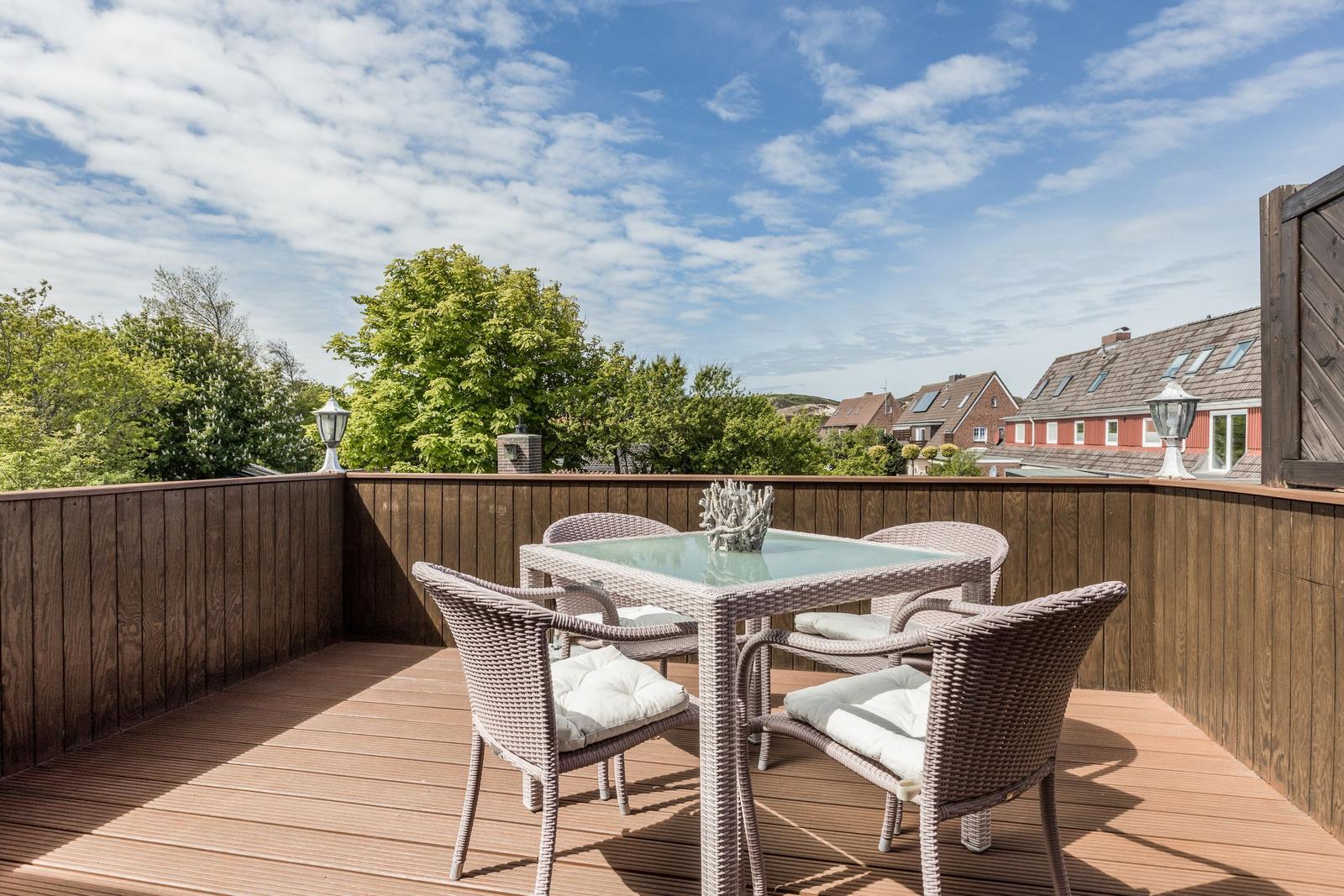 Terrasse mit Sitzgruppe und Holzgeländer. Blick auf Bäume und Häuser.
