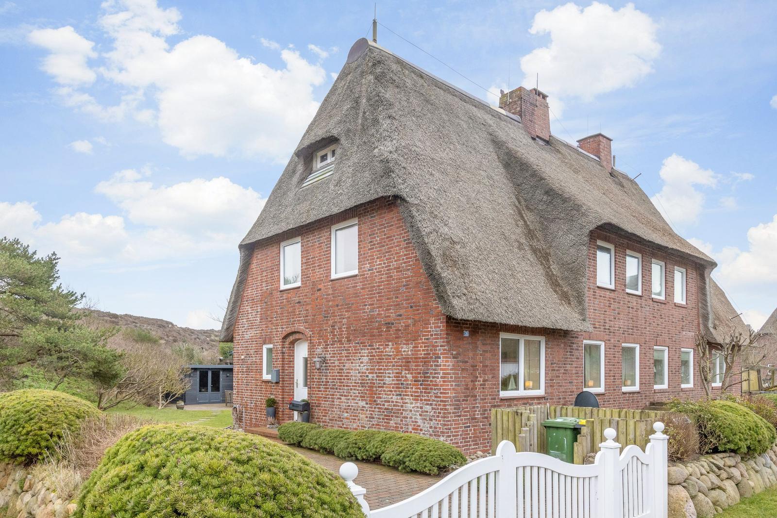 Red brick house with thatched roof and white gate