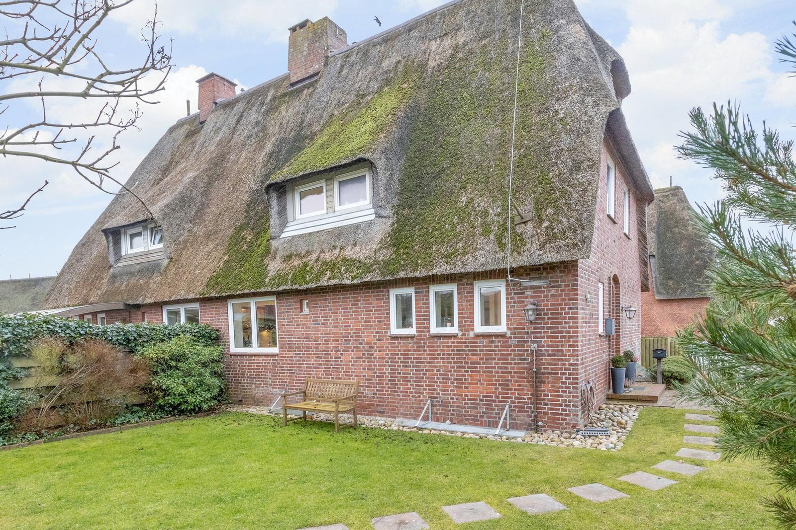 Red brick house with thatched roof and garden.
