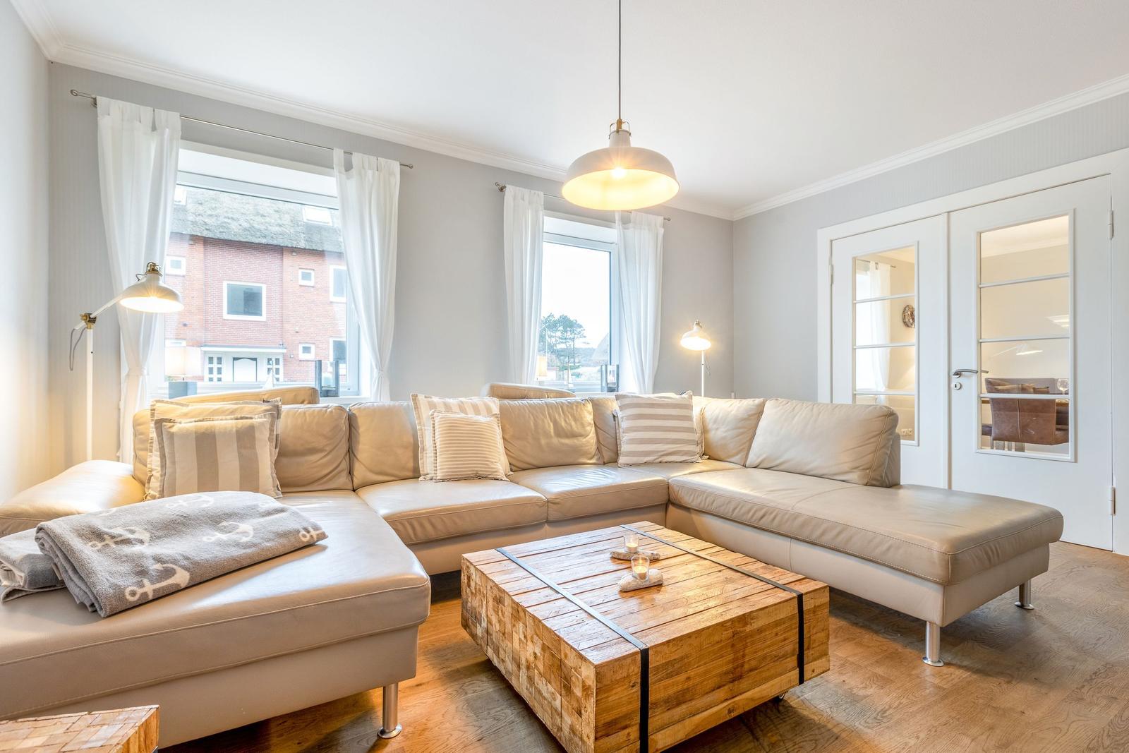 Living room with L-shaped sofa, wooden table, and windows.