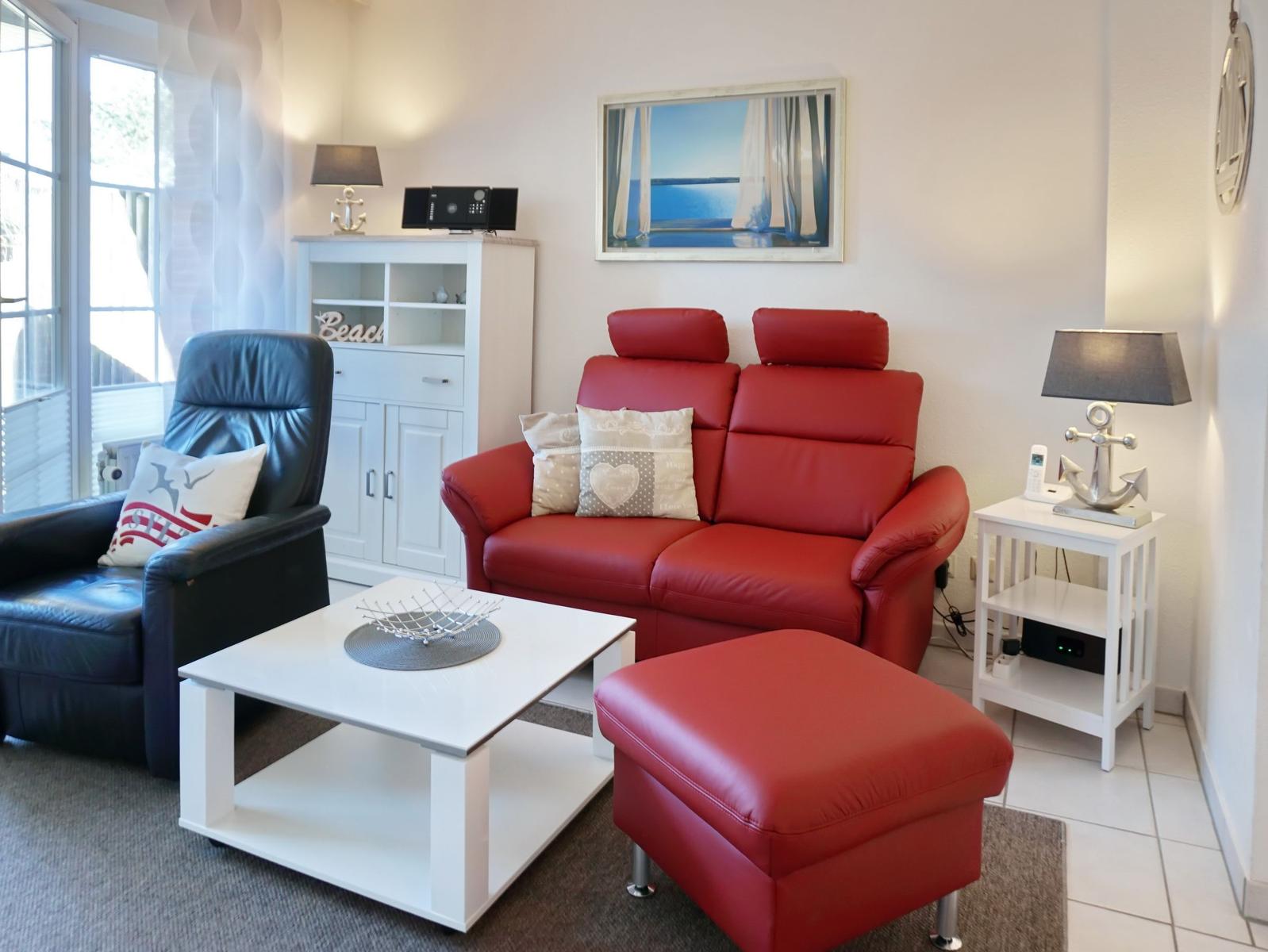 Red sofa with footstool, black armchair, white coffee table, and wall art.