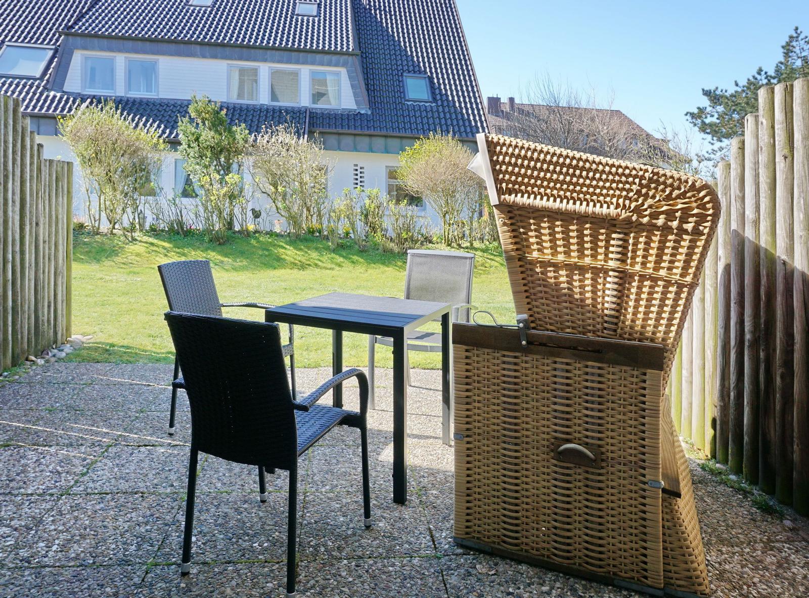 Terrace with table, chairs, and lounge chair. Background: house and garden.