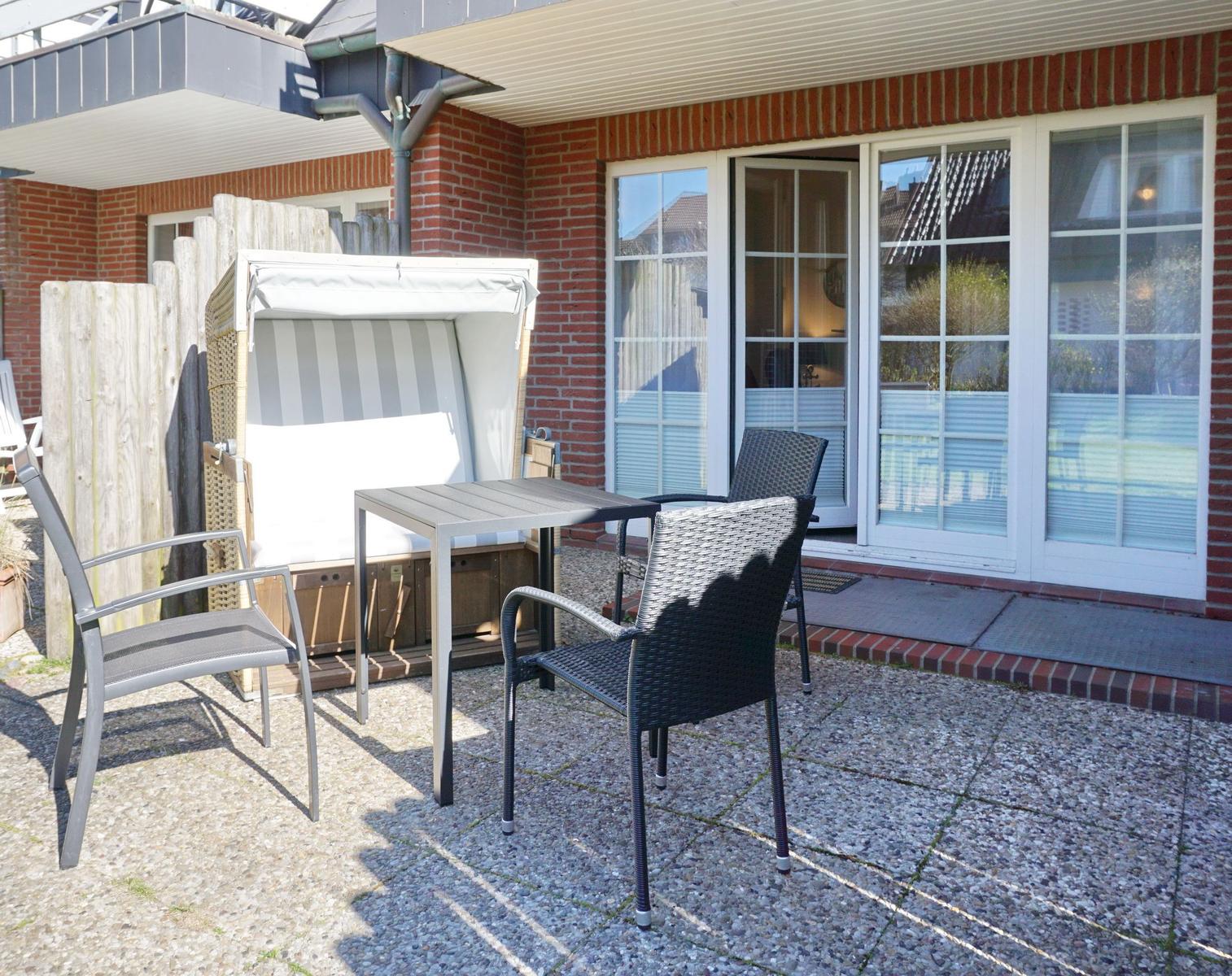 Terrace with table, chairs, and beach chair in front of house with windows.