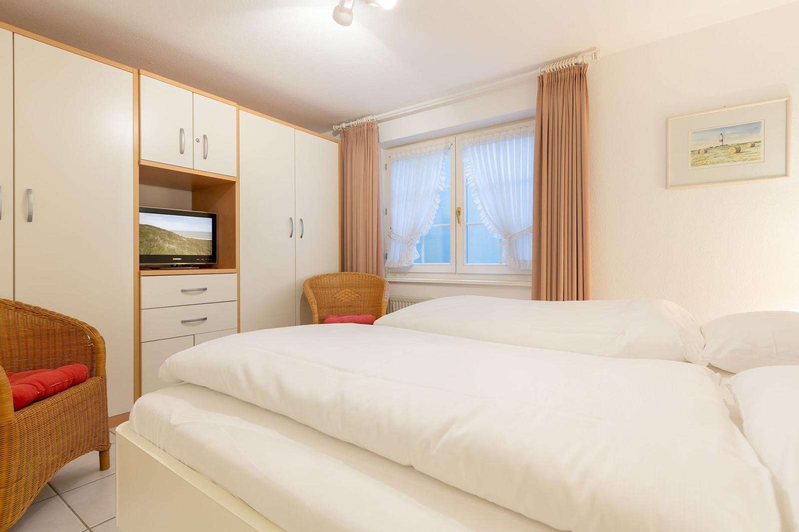 Bedroom with double bed, TV, and window with curtains.