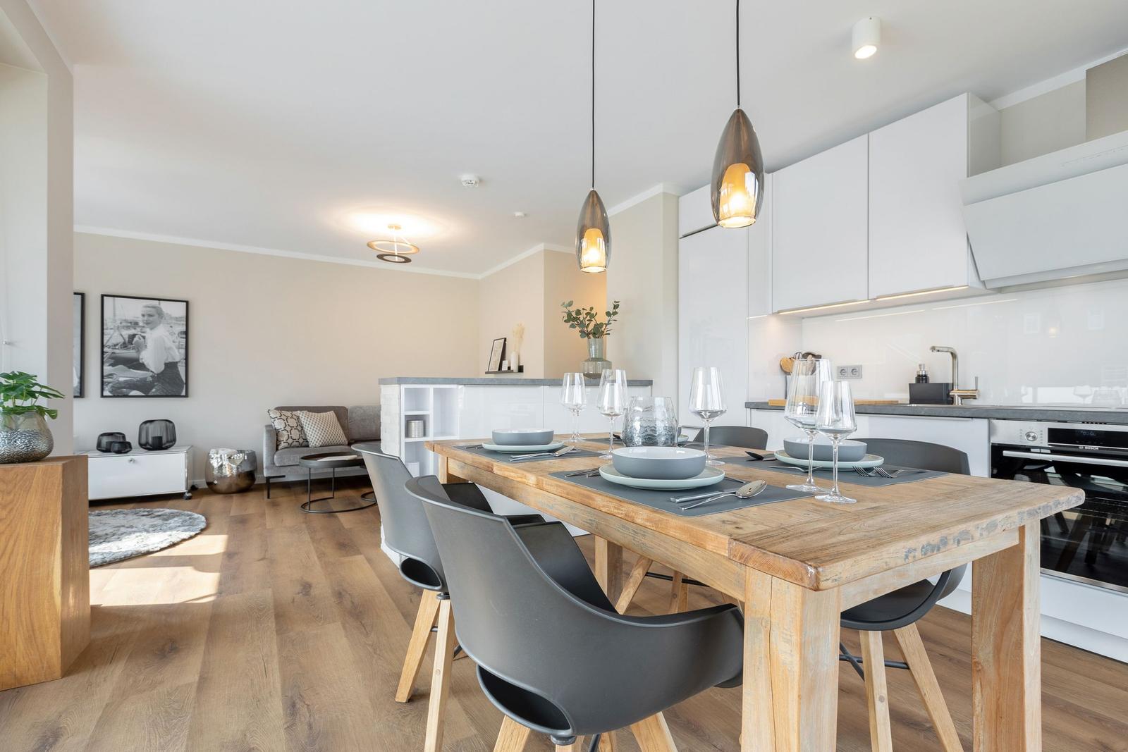 Essbereich mit Holztisch und Stühlen, Küche mit weißen Schränken und Esszimmer im Hintergrund.