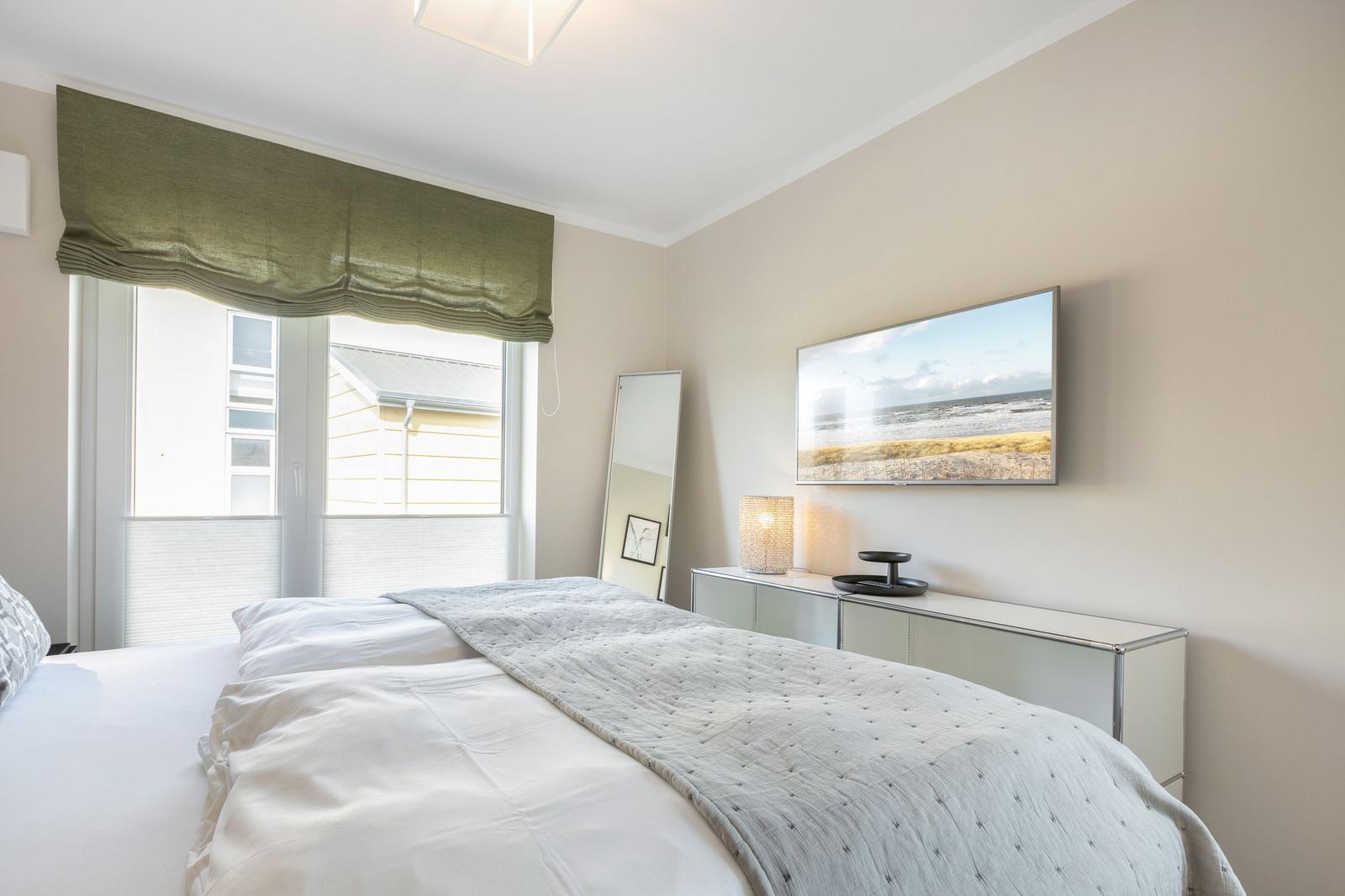 Schlafzimmer mit Bett, Fenster, Spiegel und Wandbild.