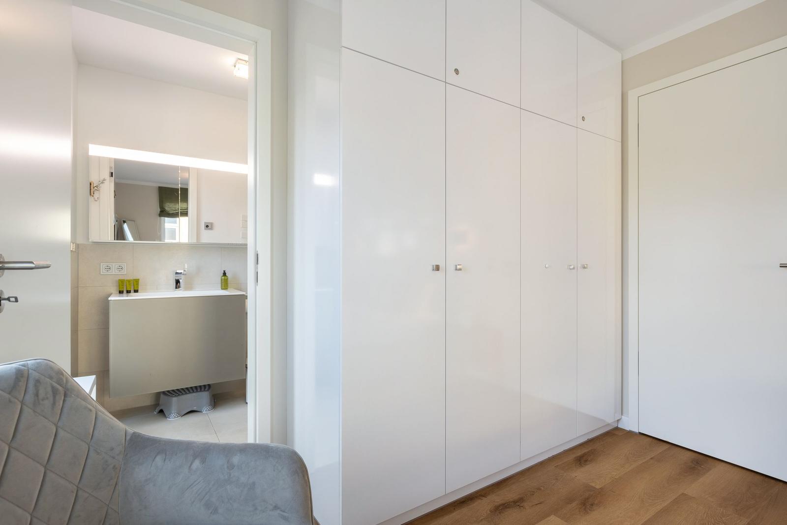 Schlafzimmer mit weißem Schrank und Blick in das Bad.