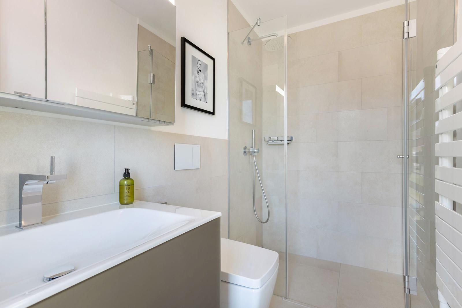 Bad mit Dusche, Waschbecken und Toilette. Fliesenwand und Spiegel sichtbar.