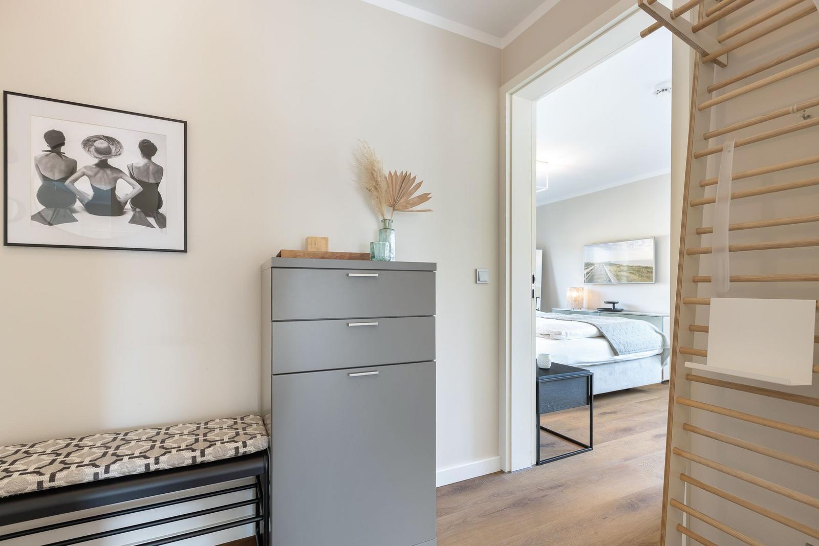 Schlafzimmer mit Kleiderschrank, Wandbild und Holzstange. Blick in Schlafbereich mit Bett und Nachttisch.
