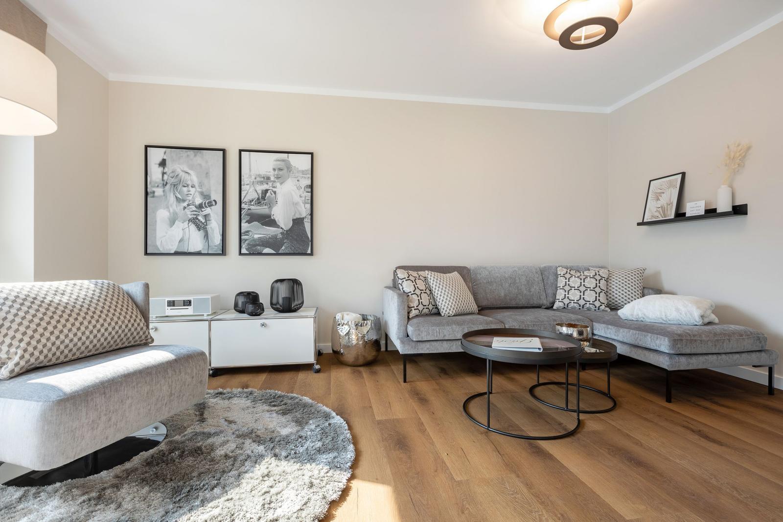 Wohnzimmer mit grauem Sofa, Holzboden und Wandbildern.