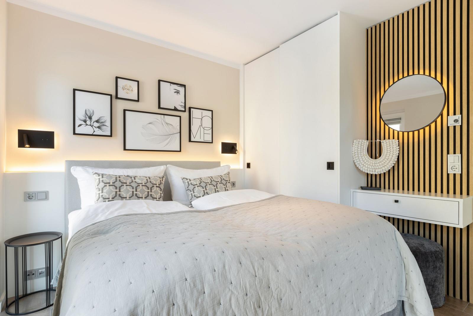 Schlafzimmer mit Bett, Wandbildern und Schminktisch mit Spiegel.