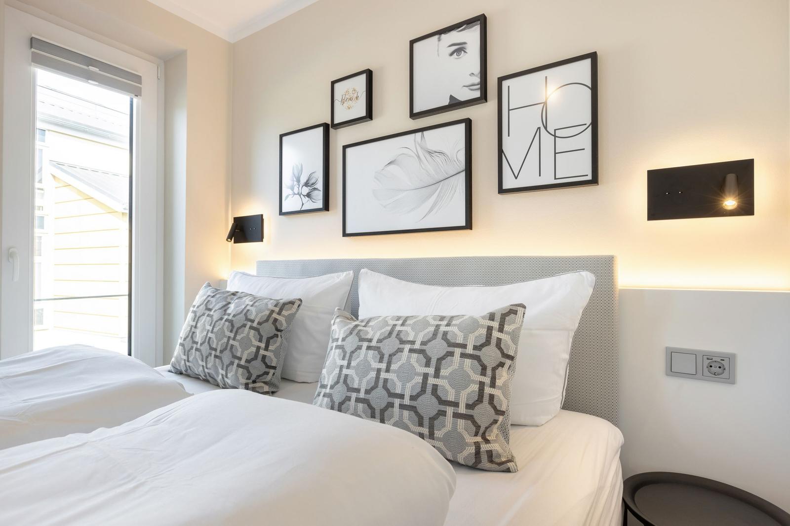 Schlafzimmer mit Bett, Wandbildern und Fenster. Beleuchtung an der Wand.