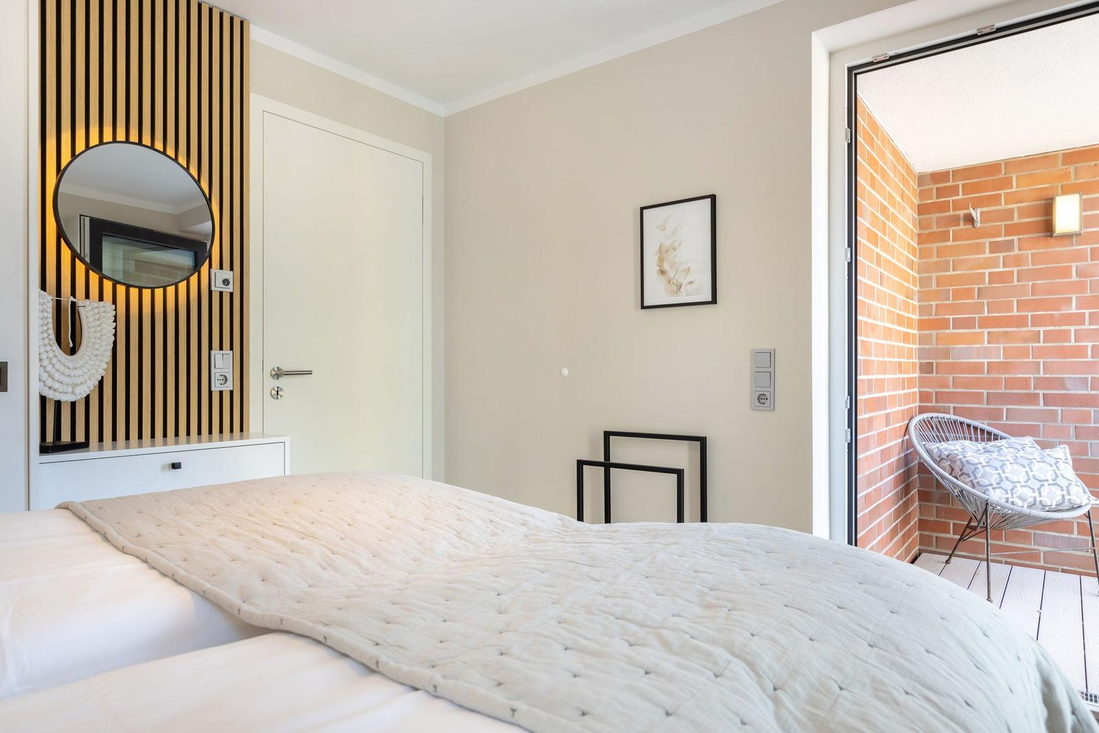 Schlafzimmer mit Bett, Spiegel und Zugang zu Balkon mit Stuhl