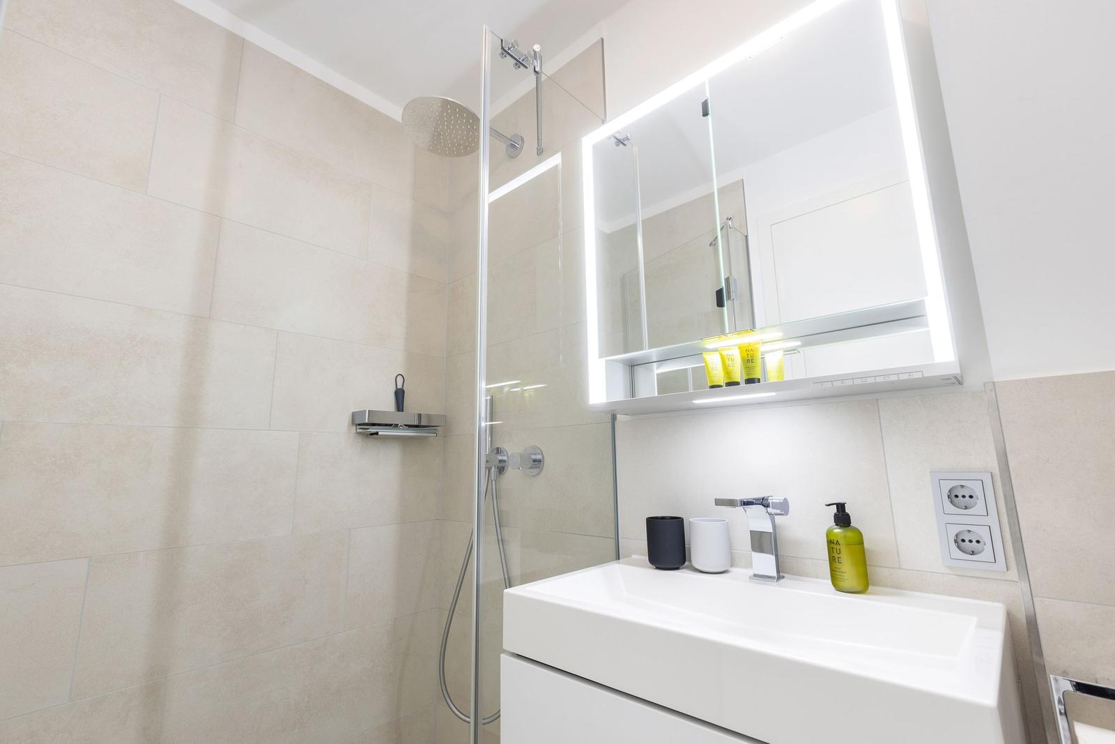 Badezimmer mit Dusche, Waschbecken und beleuchtetem Spiegelschrank.