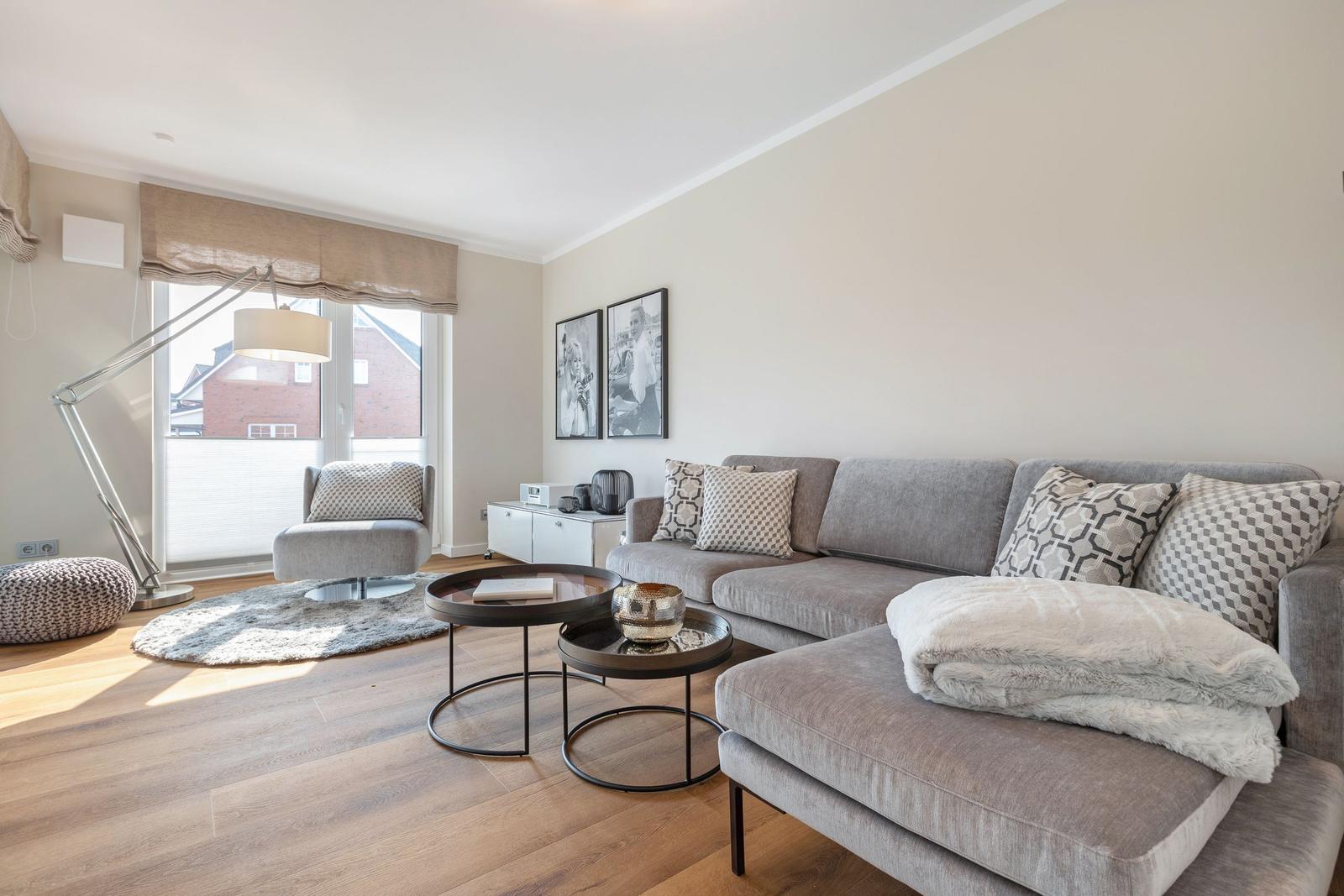 Wohnzimmer mit grauem Sofa, Couchtisch und Sessel. Holzboden und Fenster mit Rollladen.