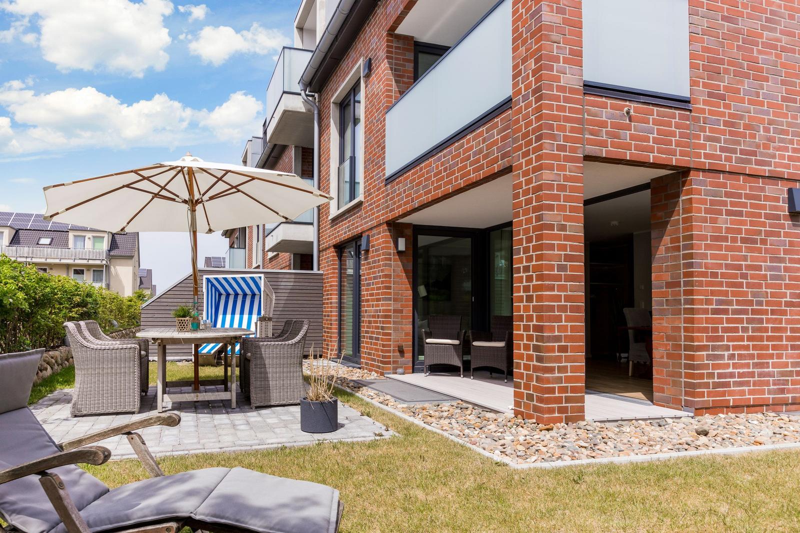 Rotes Backsteinhaus mit Terrasse und Gartenmöbeln unter Sonnenschutz.