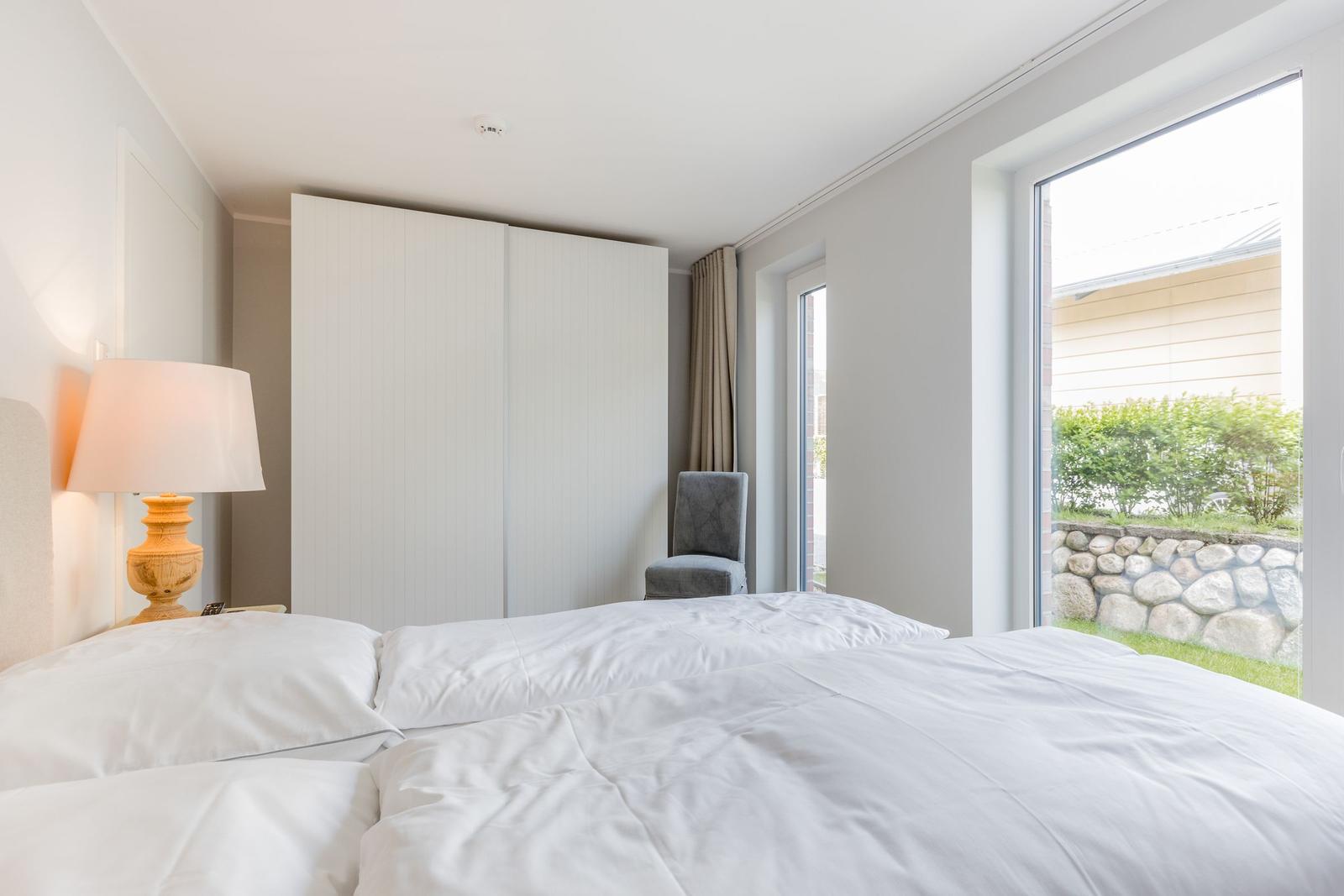 Schlafzimmer mit Doppelbett, Kleiderschrank und Fensterblick auf Garten.