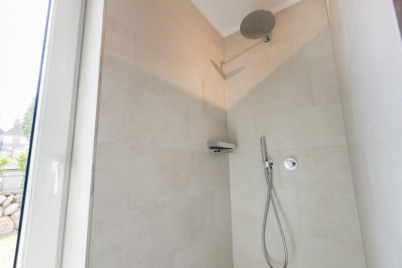 Dusche mit Duschbrause und Handbrause, Wandfliesen und Fenster.