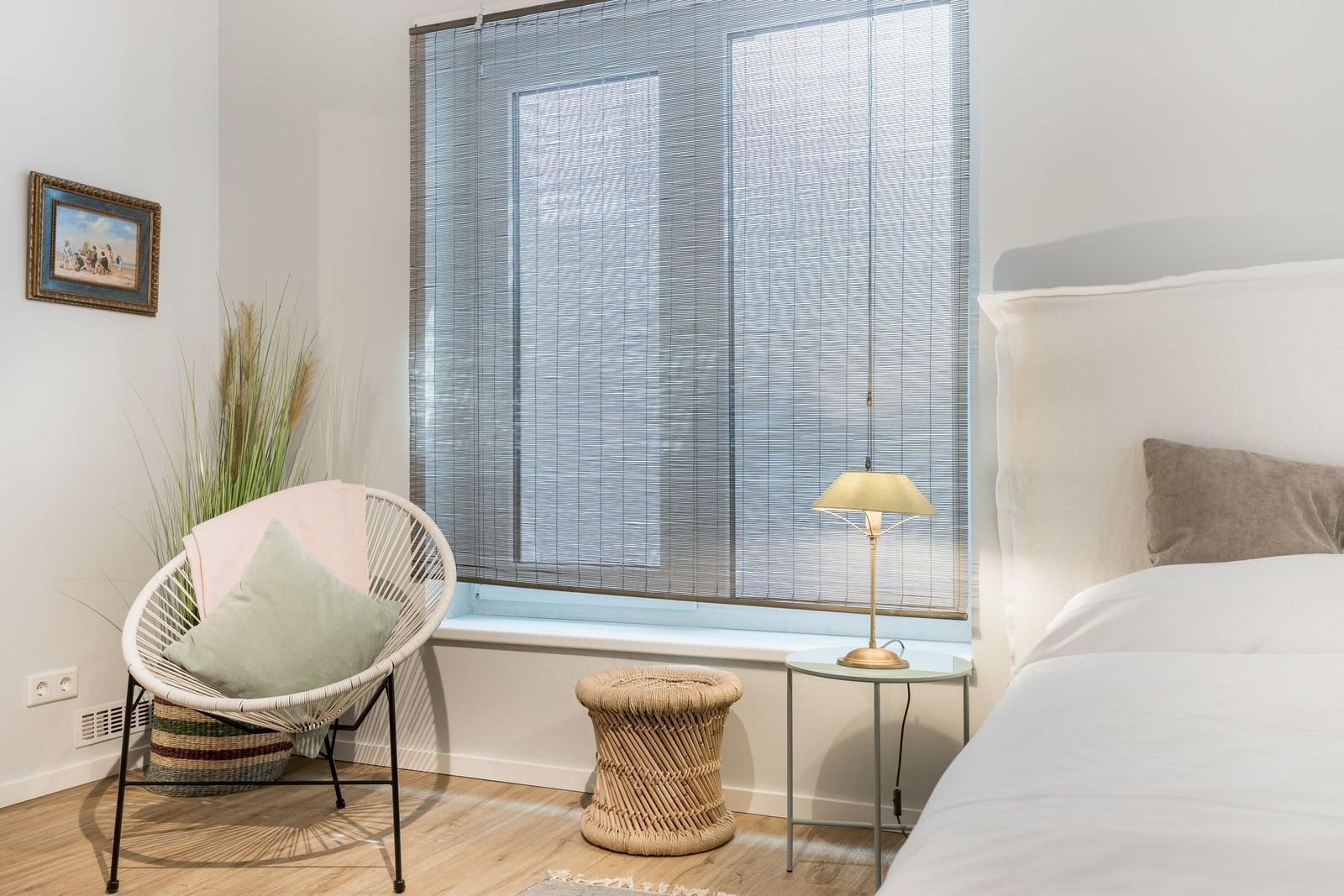 Schlafzimmer mit Bett, Stuhl und Fenster mit Jalousie.