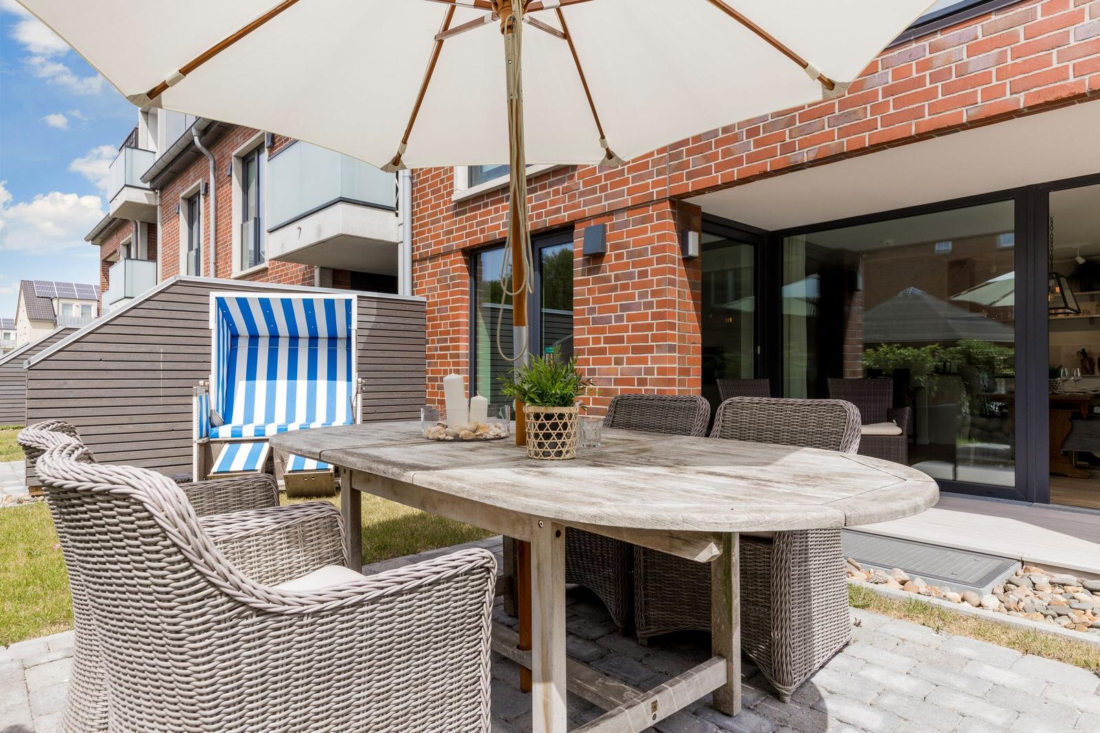 Terrasse mit Tisch, Stühlen und Sonnenschirm. Hintergrund: rote Ziegelwand und Glasfront.