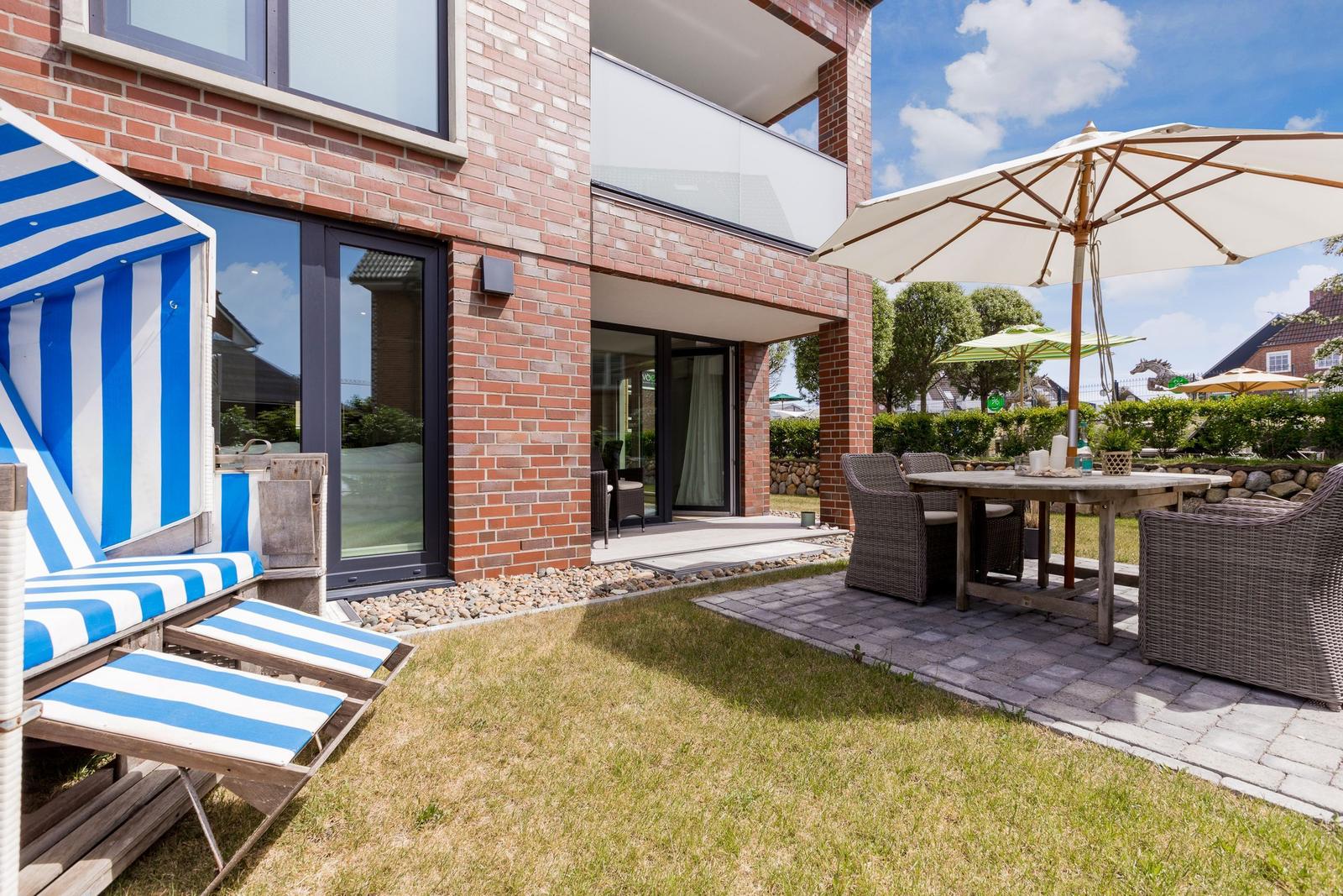Terrasse mit Sitzgruppe, Sonnenschirm und Strandkörben vor einem Haus mit Backsteinfassade.