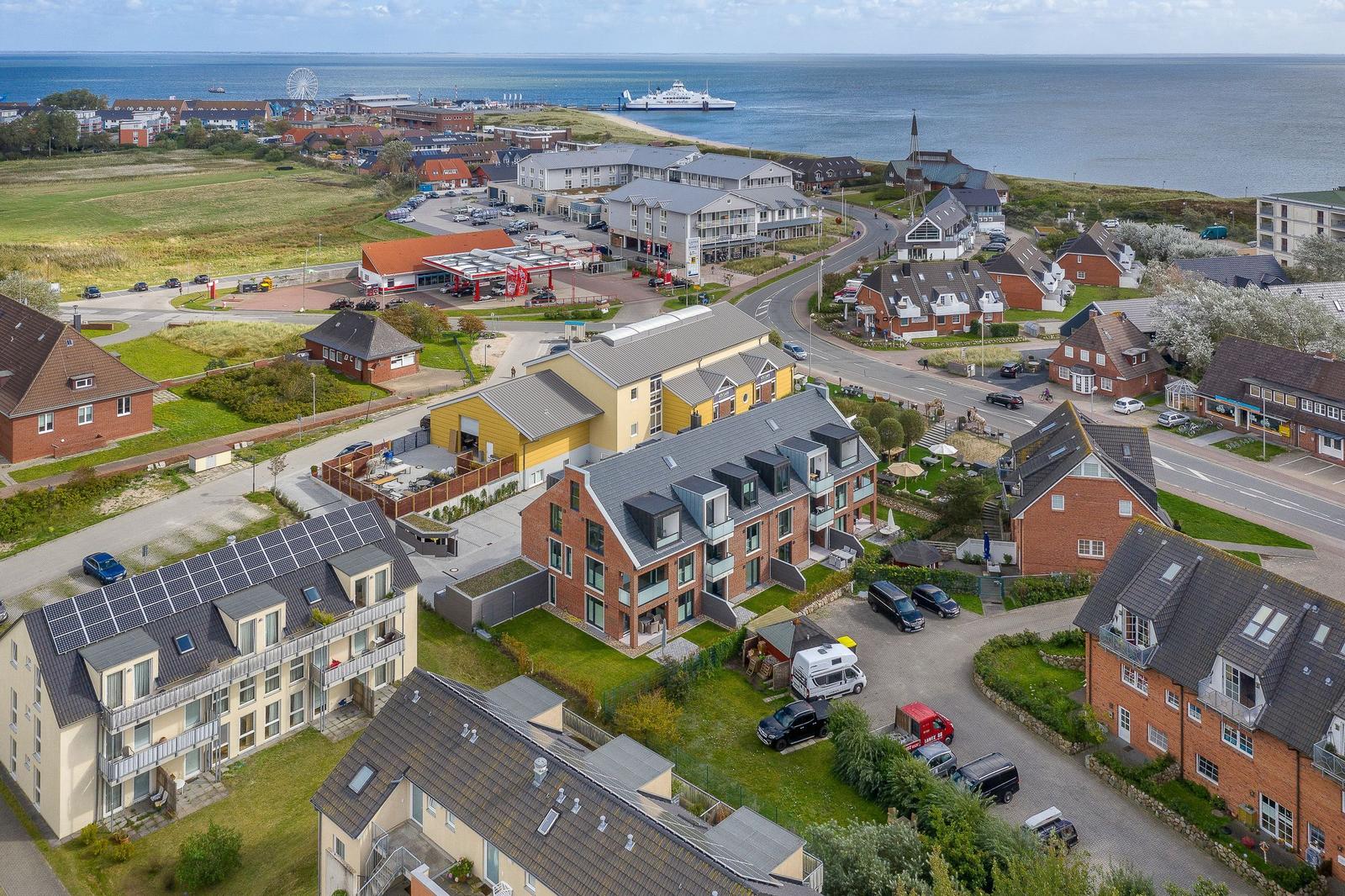 Häuser mit Dächern und Grünflächen an der Küste mit Blick aufs Meer und ein Schiff.