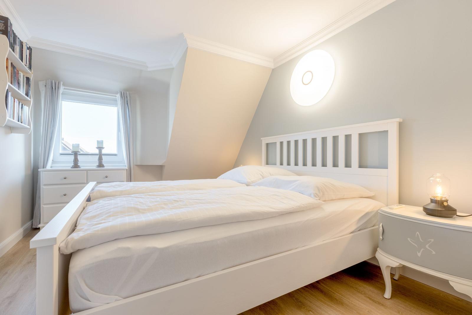 Schlafzimmer mit weißem Bett, Nachttisch und Fenster