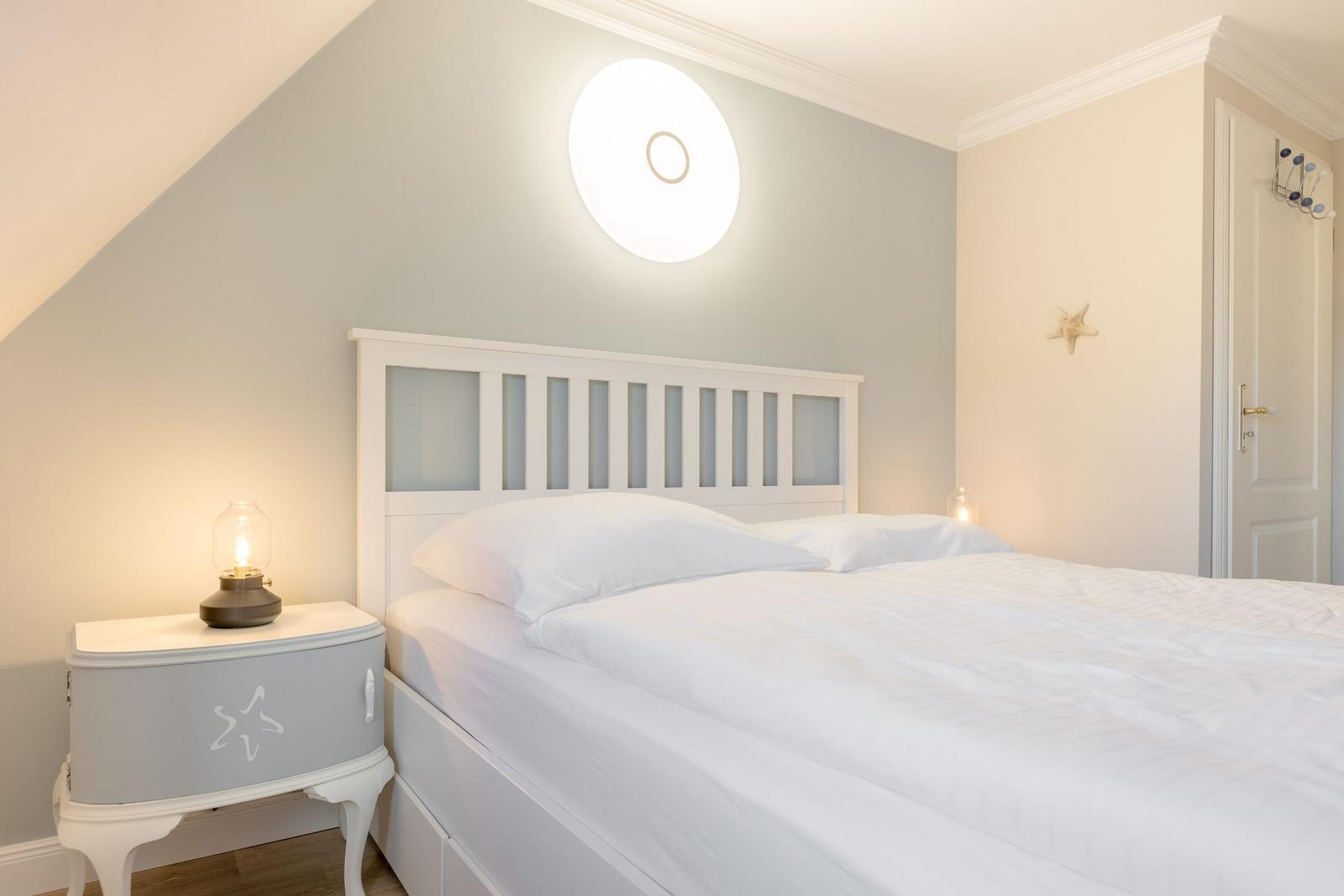 Schlafzimmer mit weißem Bett, Nachttisch und Wandlampe