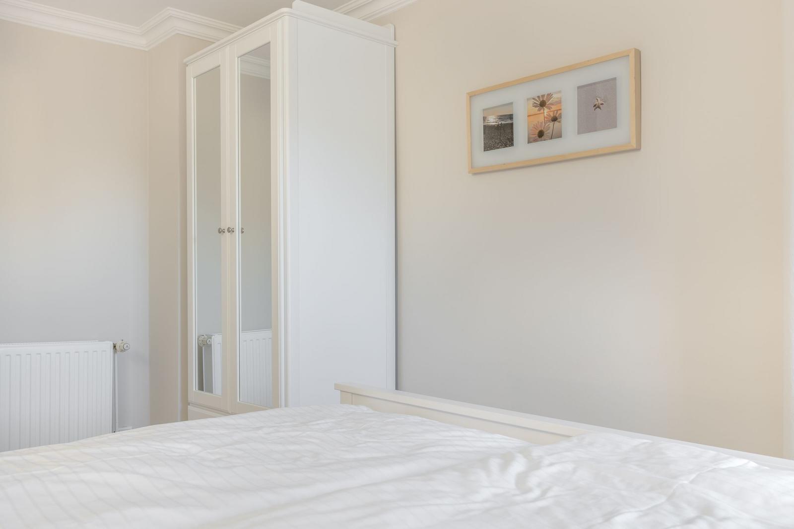 Schlafzimmer mit weißem Bett, Kleiderschrank und Wandbild.