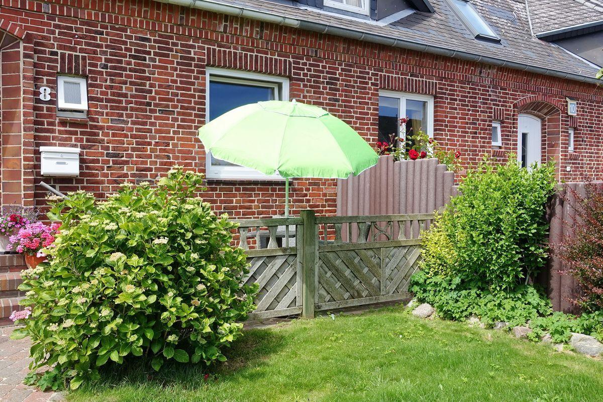 Rotes Backsteinhaus mit grünem Sonnenschirm und gepflegtem Garten.