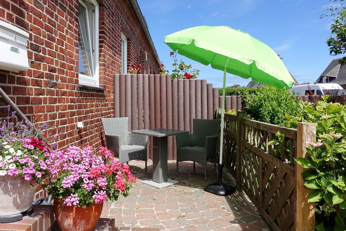 Terrasse mit grünem Sonnenschirm, Tisch, Stühlen und Blumenpflanzen.