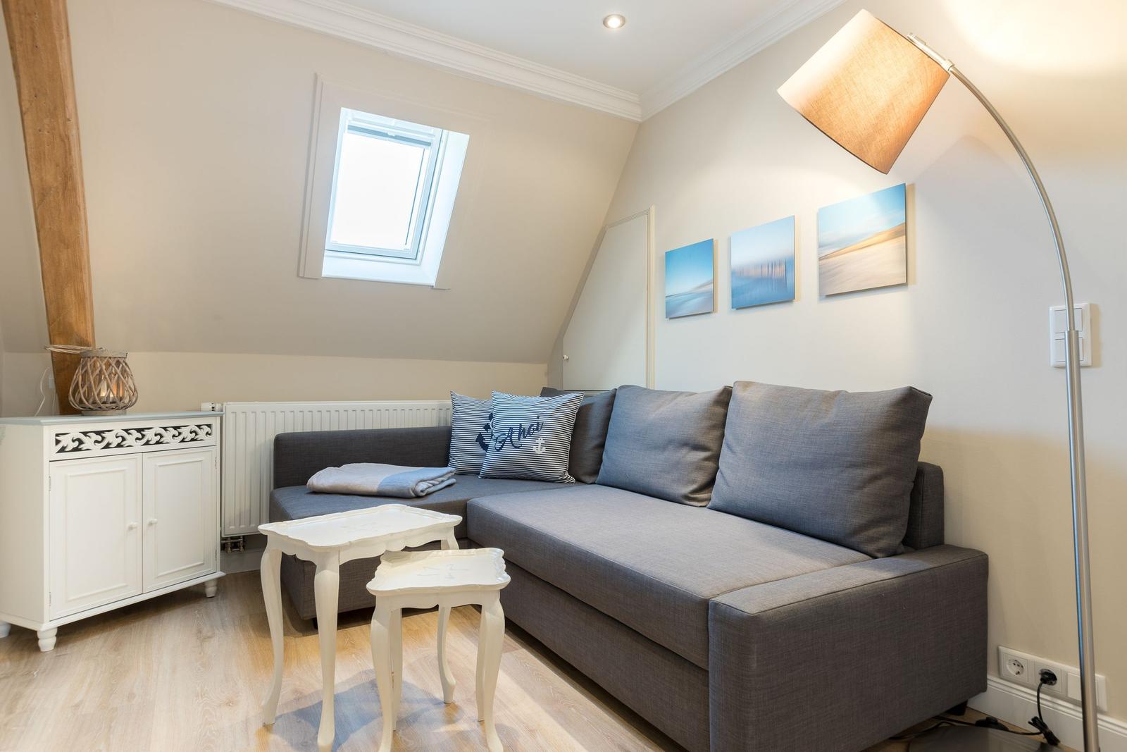 Wohnzimmer mit grauem Sofa, weißen Tischen und Fenster