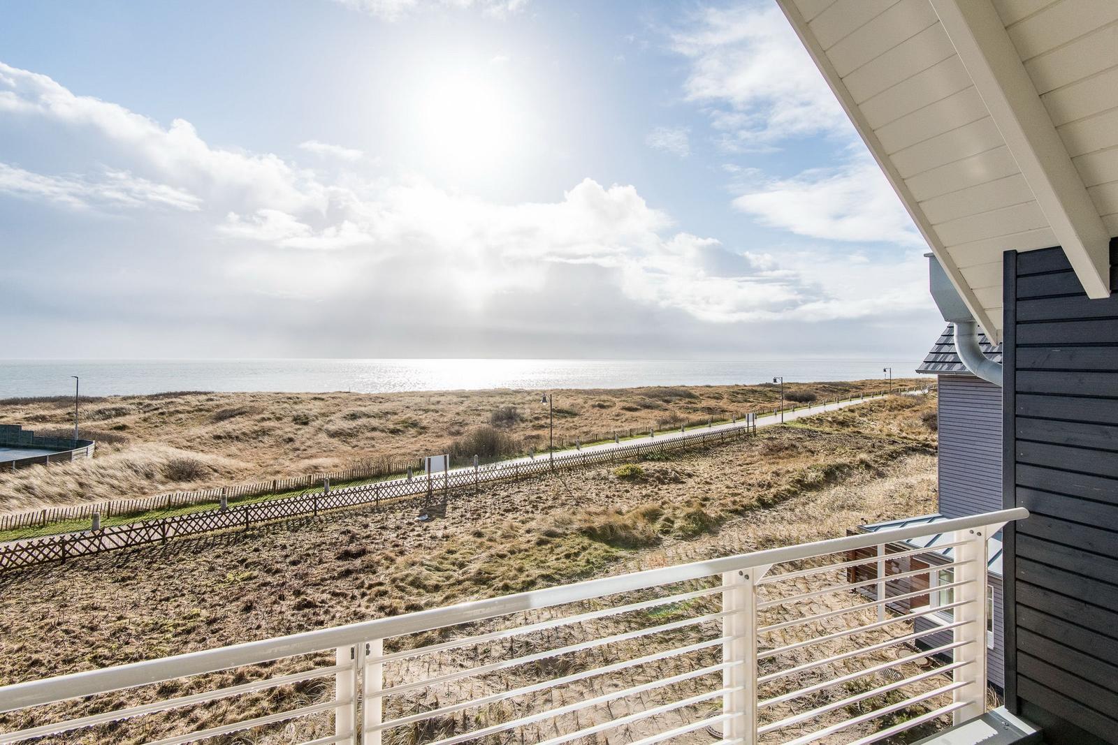 Blick von Balkon auf Strand und Meer unter blauem Himmel mit weißen Wolken.