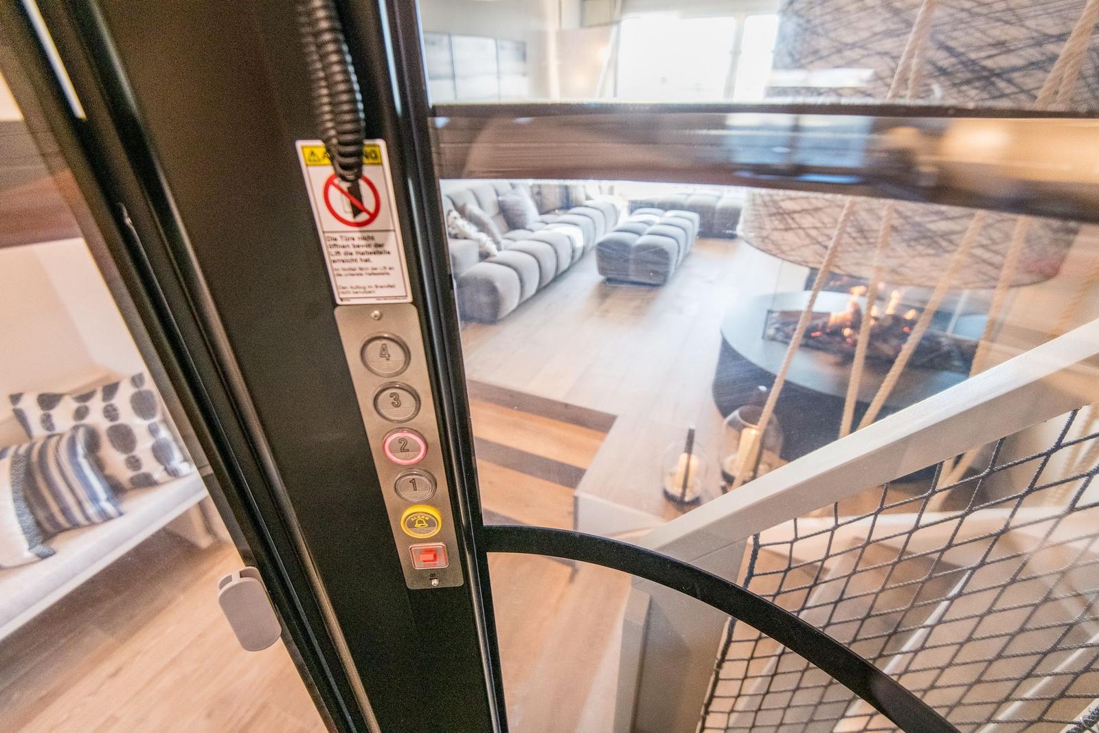 Lift mit Tastenfeld zeigt Blick auf Wohnbereich mit Sofa und Kamin.