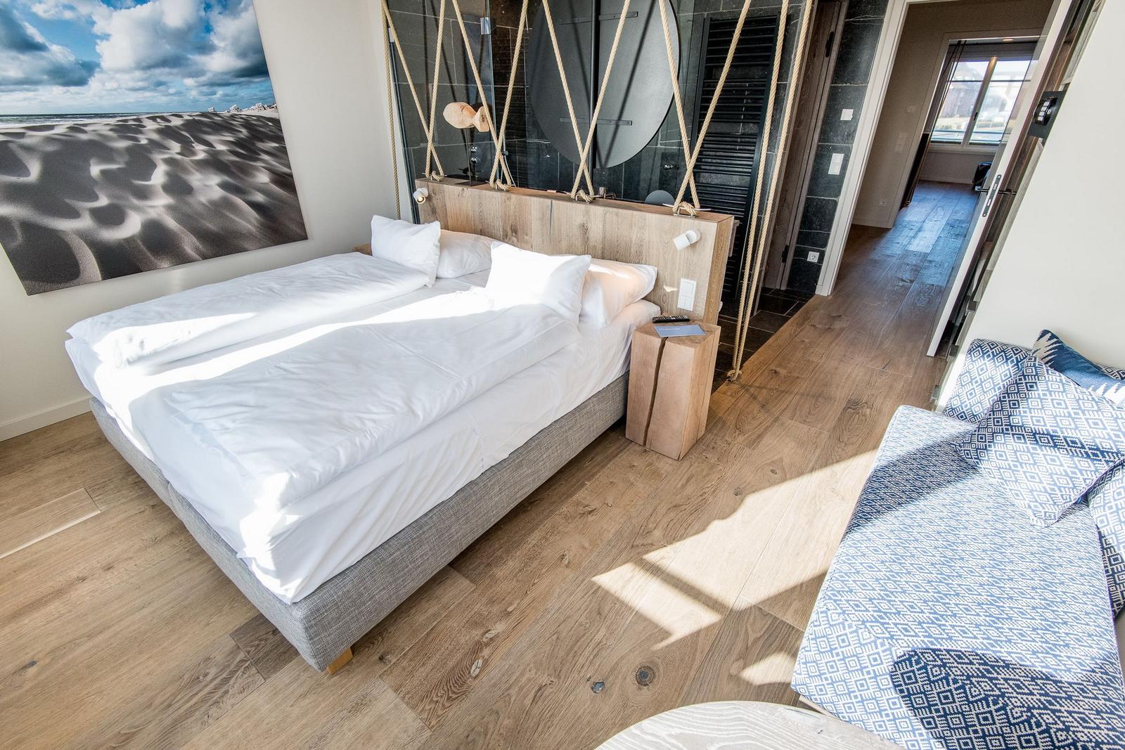 Schlafzimmer mit Doppelbett, Holzboden und Strandbild an der Wand.