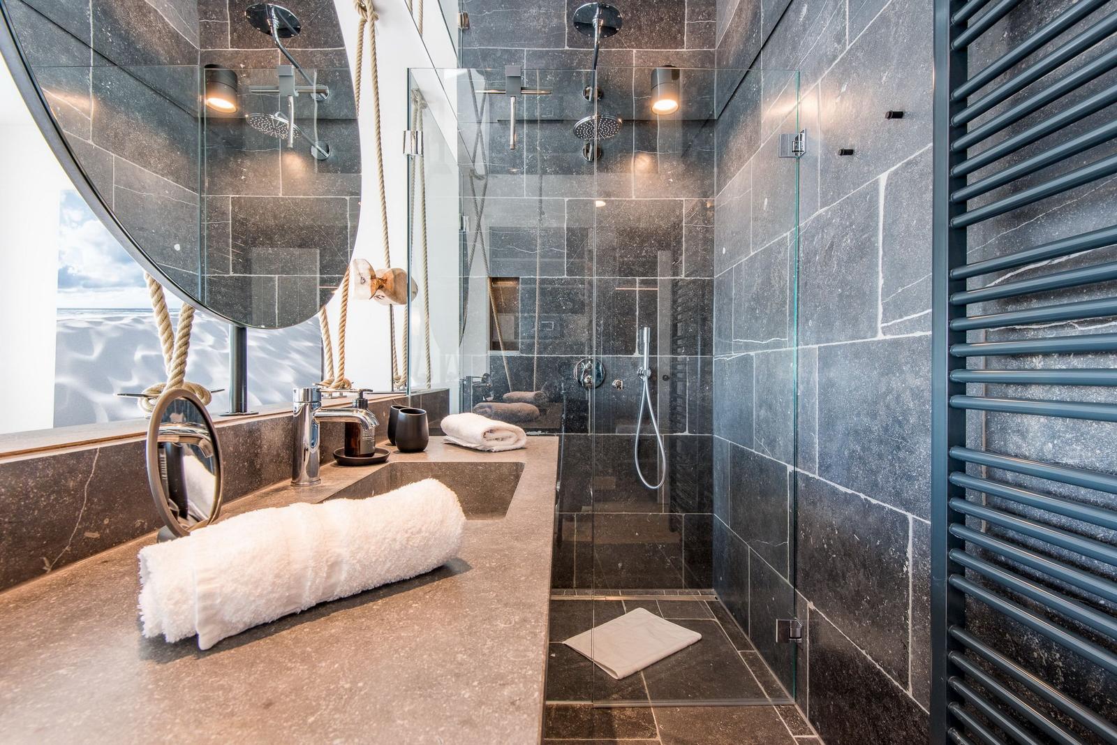 Dusche mit Glaswand, dunklen Steinwänden und Badewanne mit Seilzug.