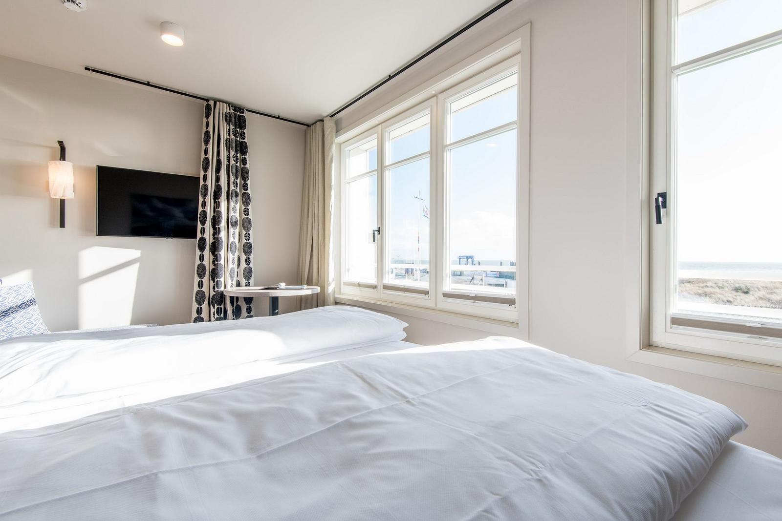 Zimmer mit Doppelbett, TV und Blick aufs Meer.