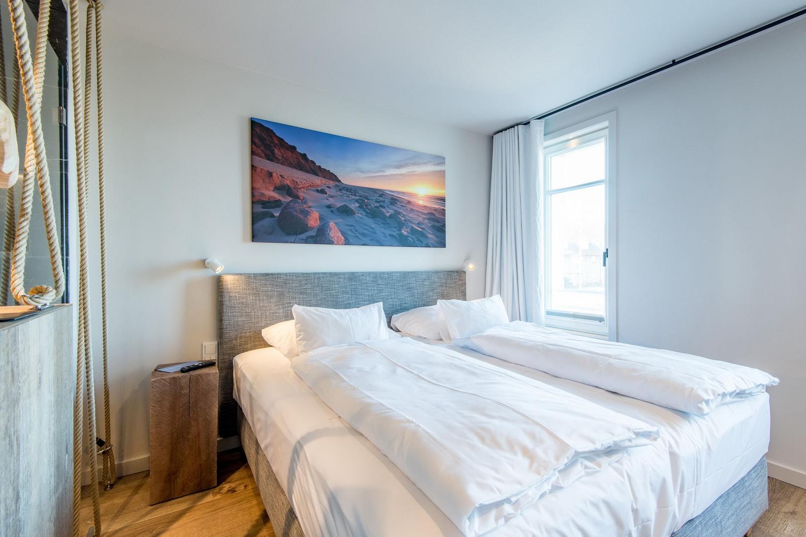 Schlafzimmer mit Doppelbett, Wandbild und Fenster.