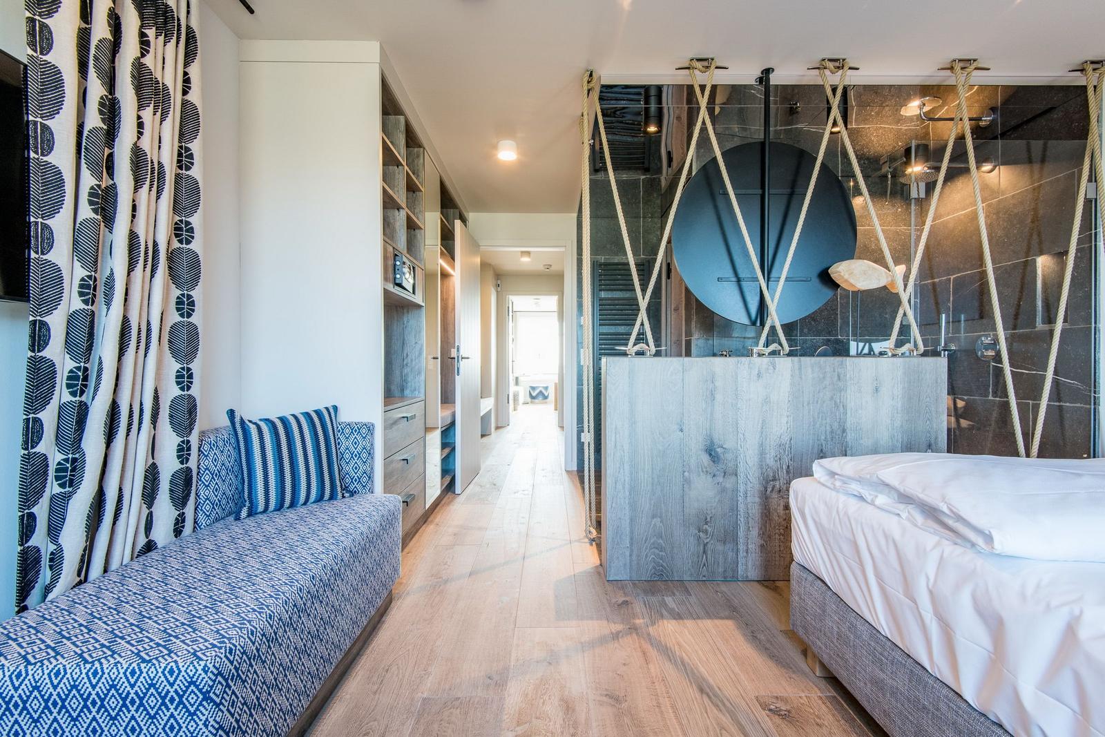 Schlafzimmer mit Bett, Sitzbank und moderner Dusche.