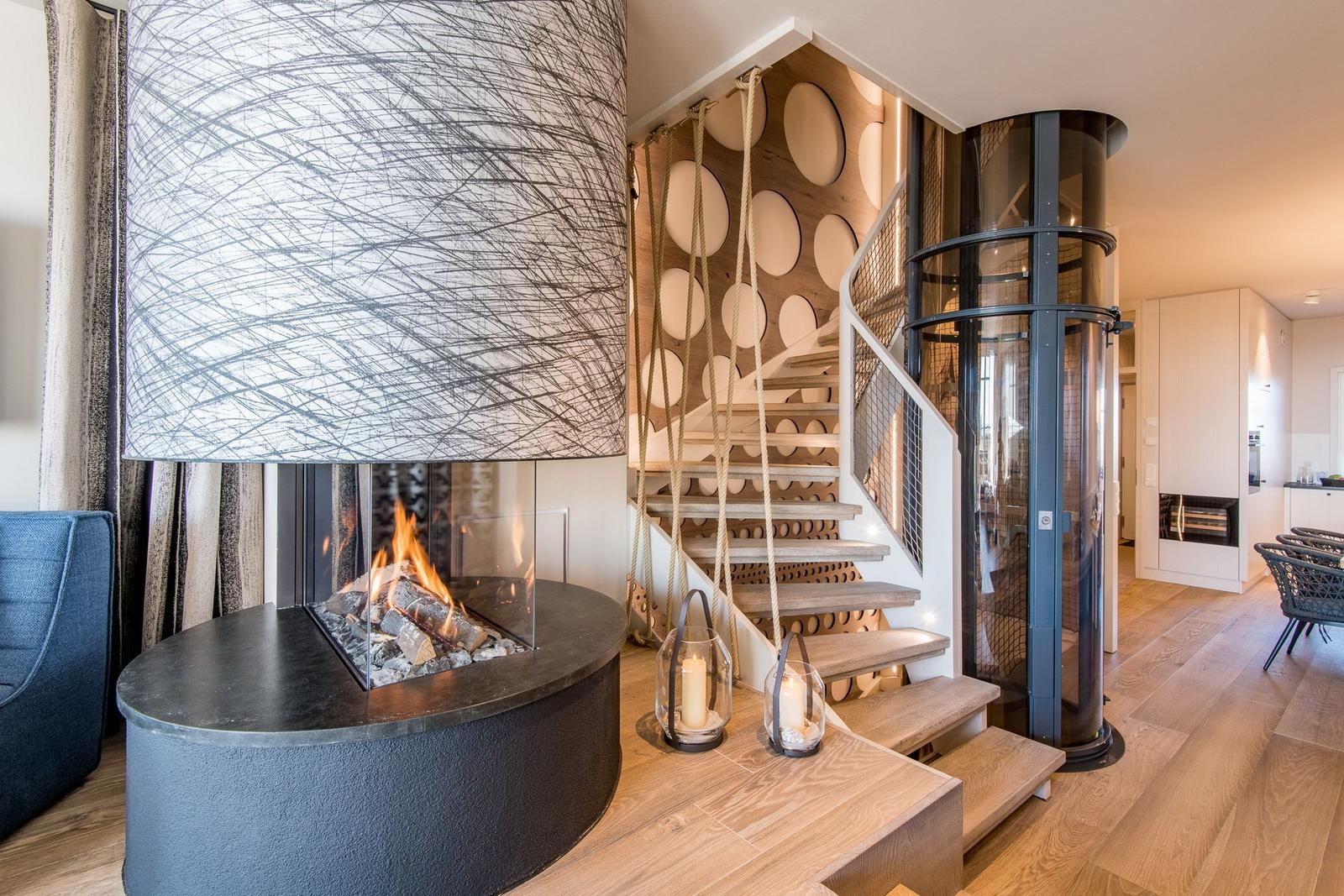 Moderne Wohnfläche mit Kamin, Holztreppe und Glaslift.
