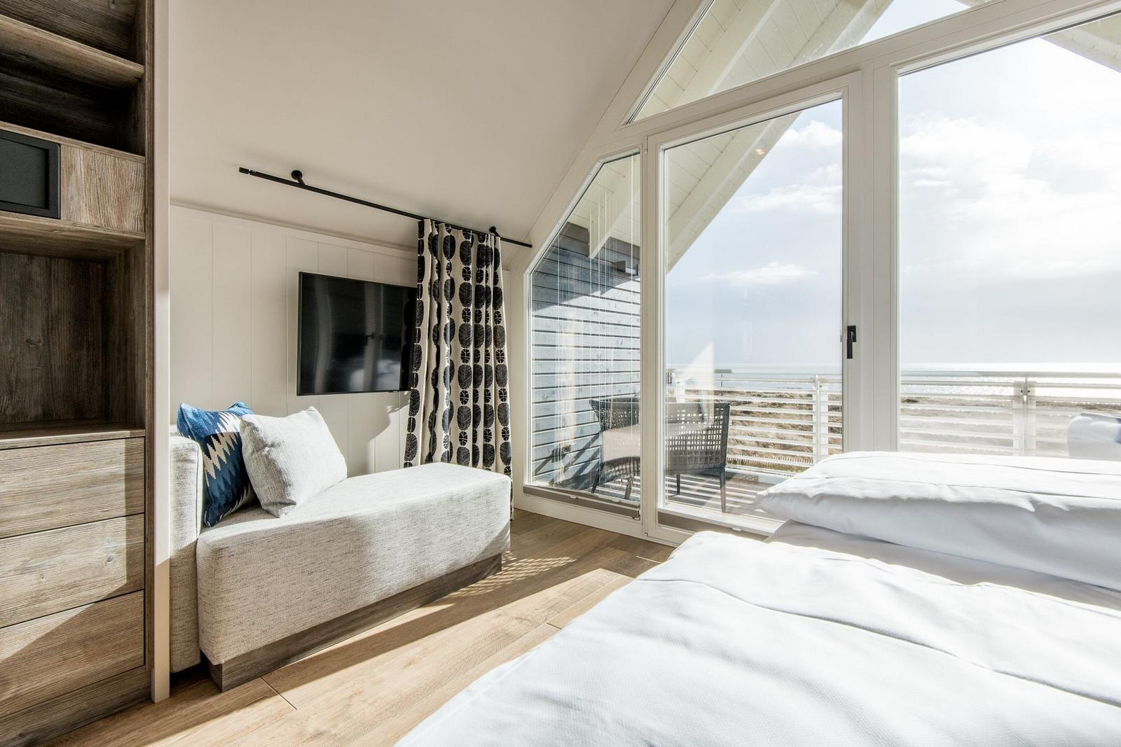 Schlafzimmer mit Blick auf die See und Balkon. Bett, Sofa und Fernseher sichtbar.