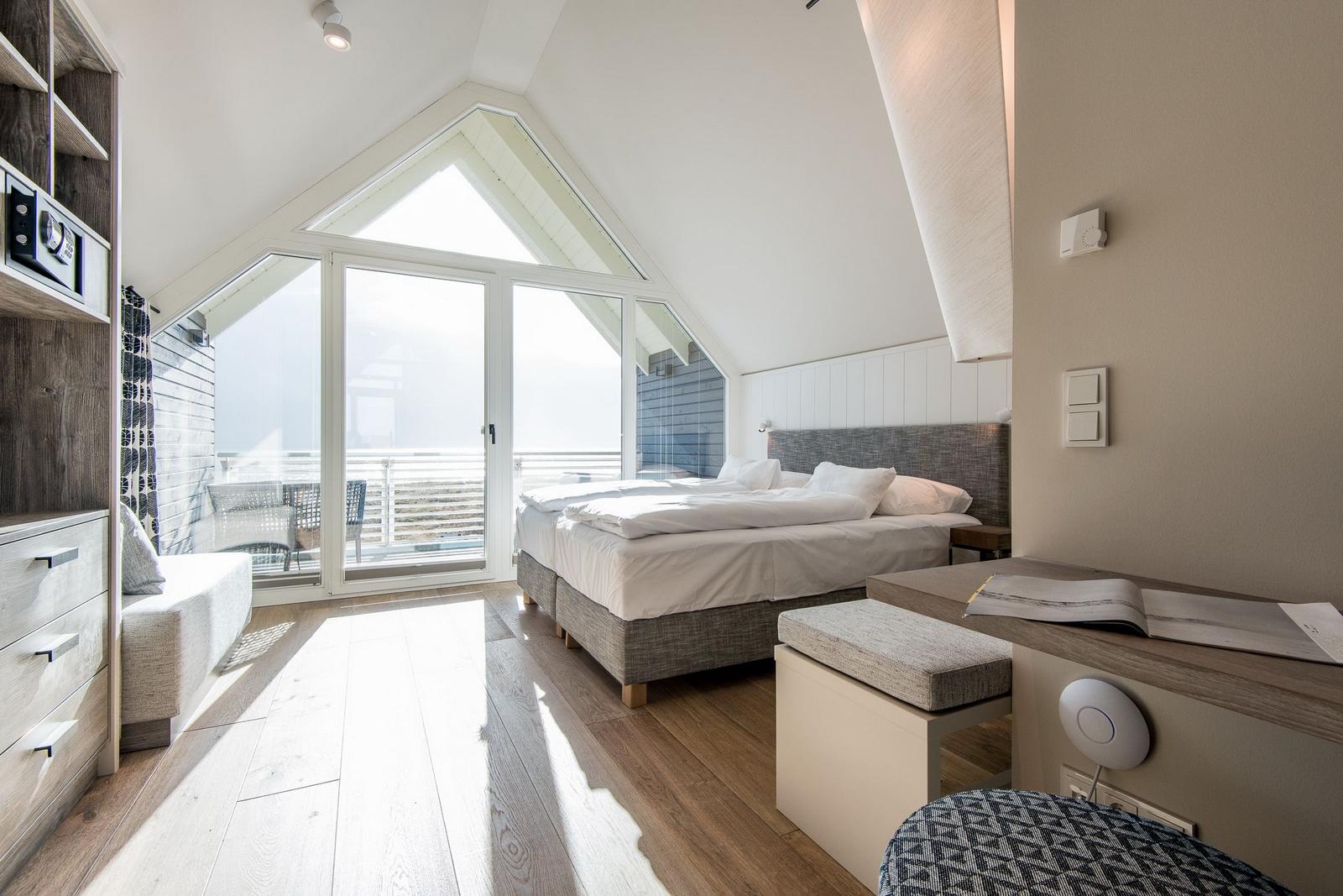 Schlafzimmer mit Doppelbett, großem Fenster und Holzboden.