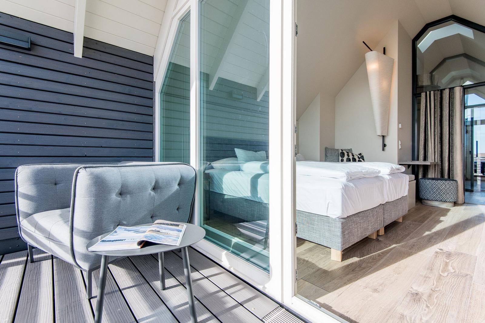 Terrasse mit Sitzgelegenheit und Blick in das Schlafzimmer mit Bett und Lampen.