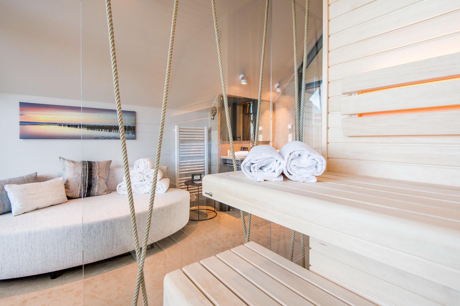Sauna mit Holzbank und Handtüchern. Im Hintergrund Sofa und Bad.