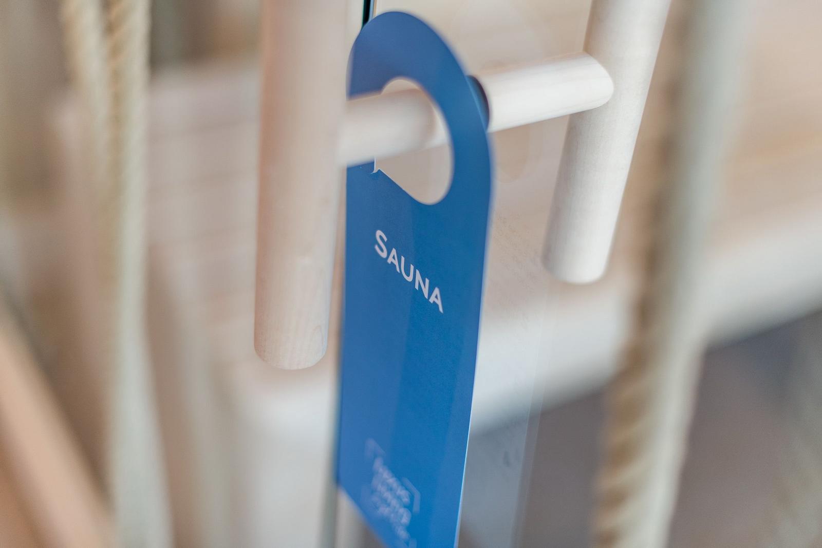 Ein blaues Schild mit der Aufschrift Sauna hängt an einem Holzgriff.