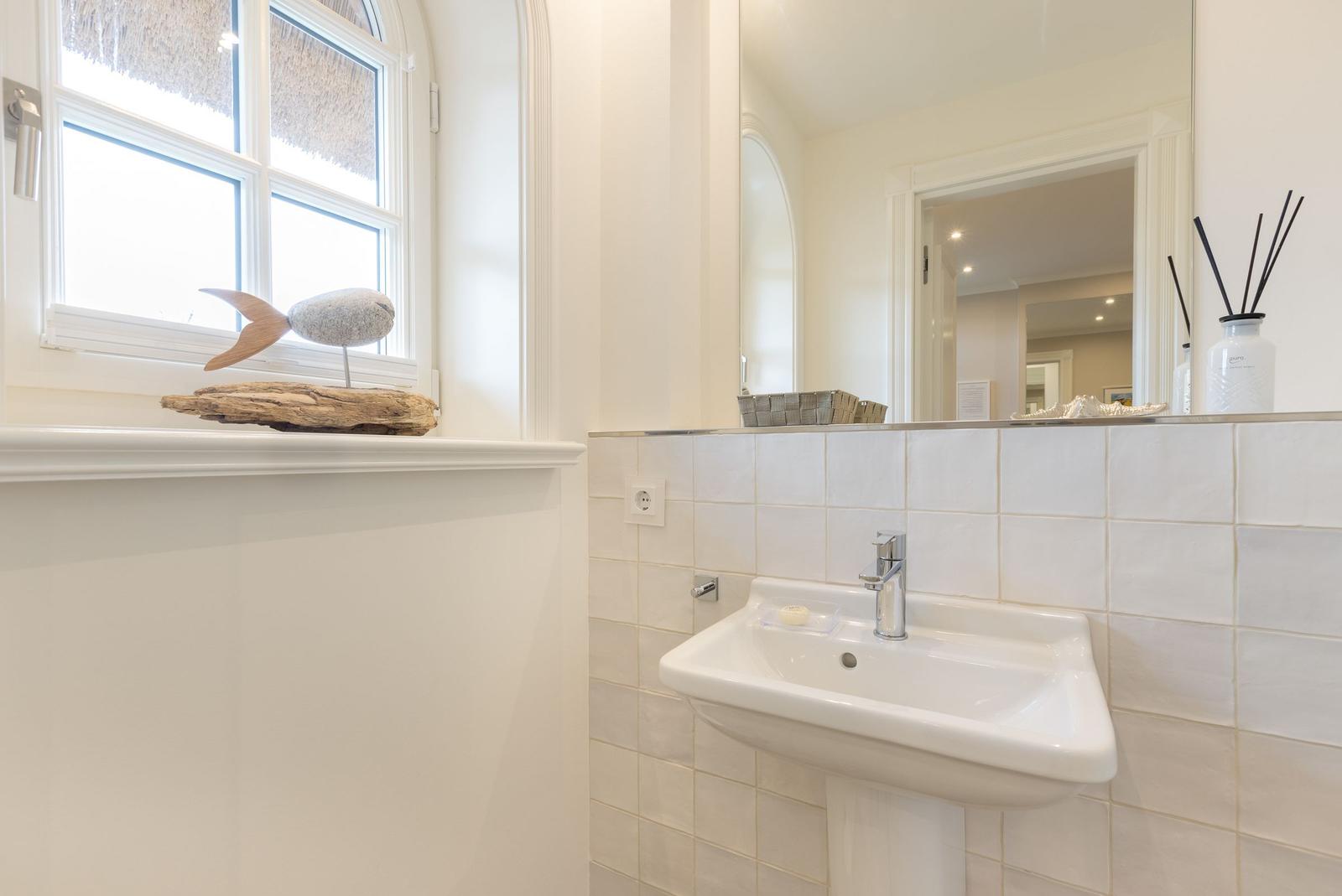 Badezimmer mit Waschbecken, Spiegel und Fenster mit dekorativen Gegenständen.