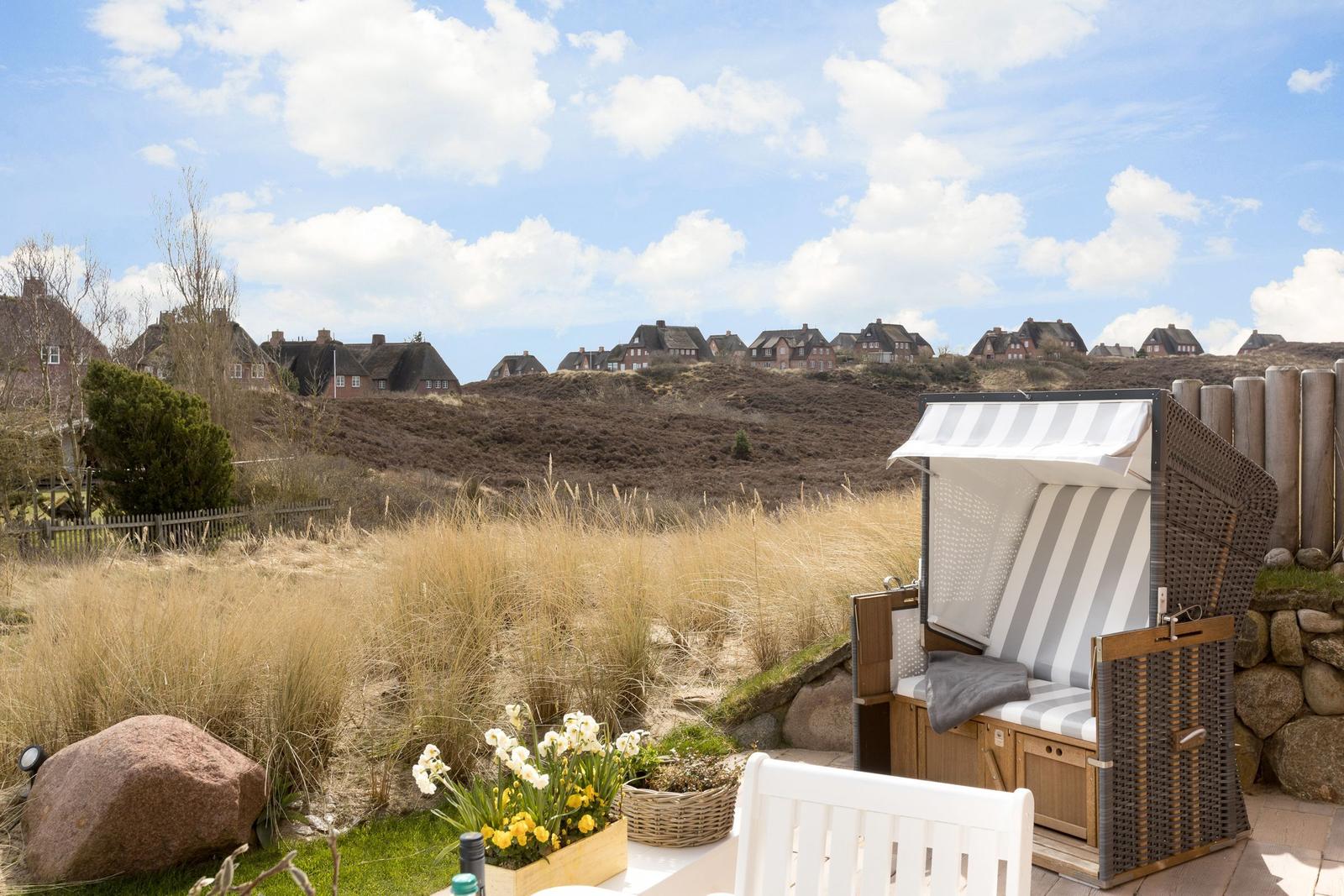 Strandkorb mit Streifenbezug, Blumen und Blick auf Häuser auf Dünen.