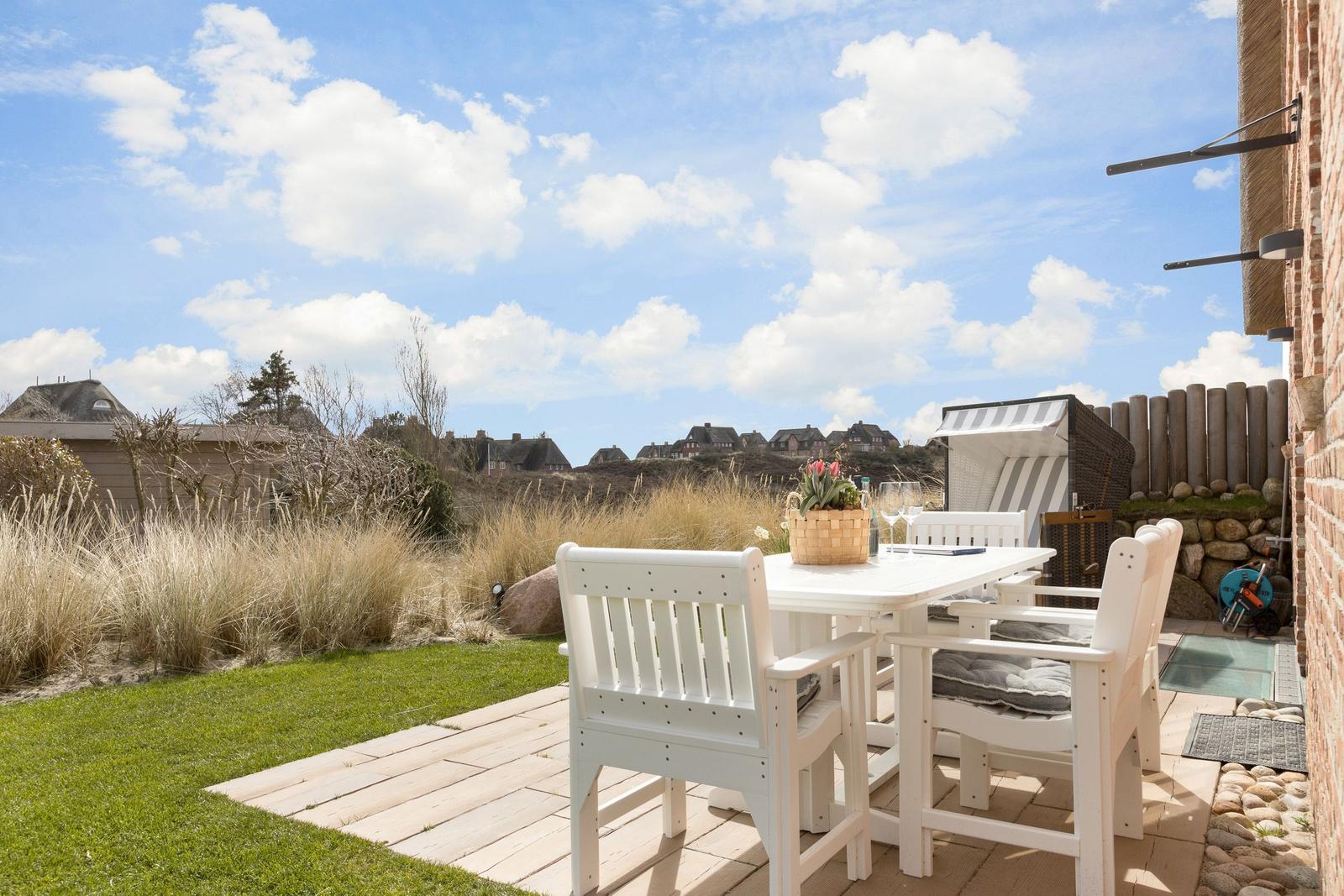 Terrasse mit weißem Tisch und Stühlen, Blick auf Gras und Häuser.
