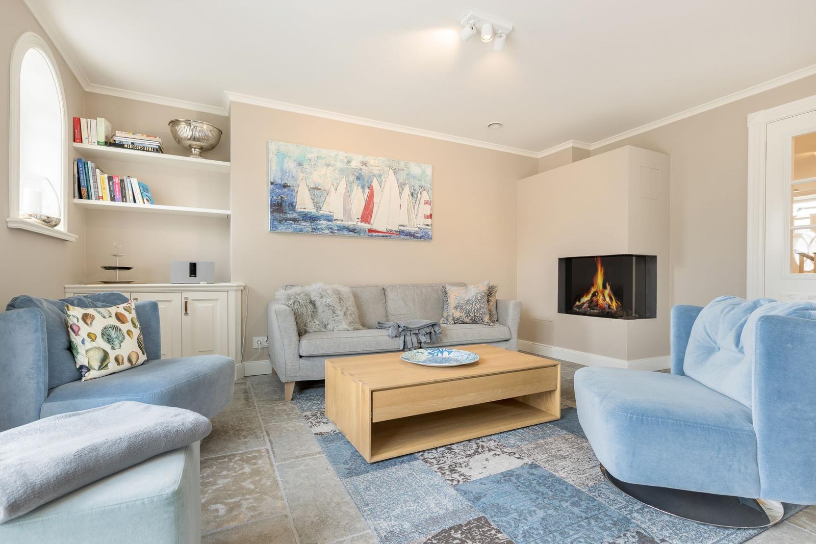 Wohnzimmer mit Sofa, zwei Sesseln, Kamin und Wandbild mit Segelbooten.